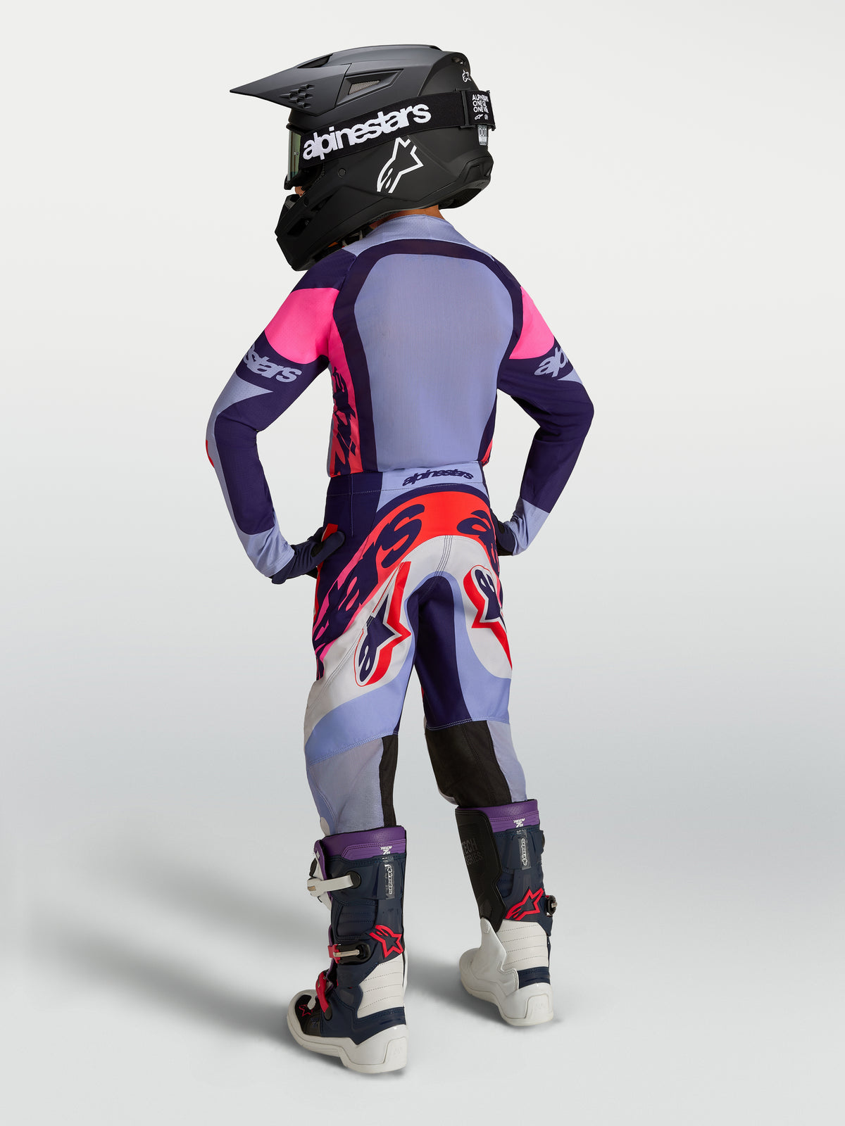 Alpinestars Juventude Supertech Dyna Gear Set, conjunto de motocross para juventude, roxo e rosa, inclui camisola, calças, botas e capacete, vista traseira com ajuste de corrida.