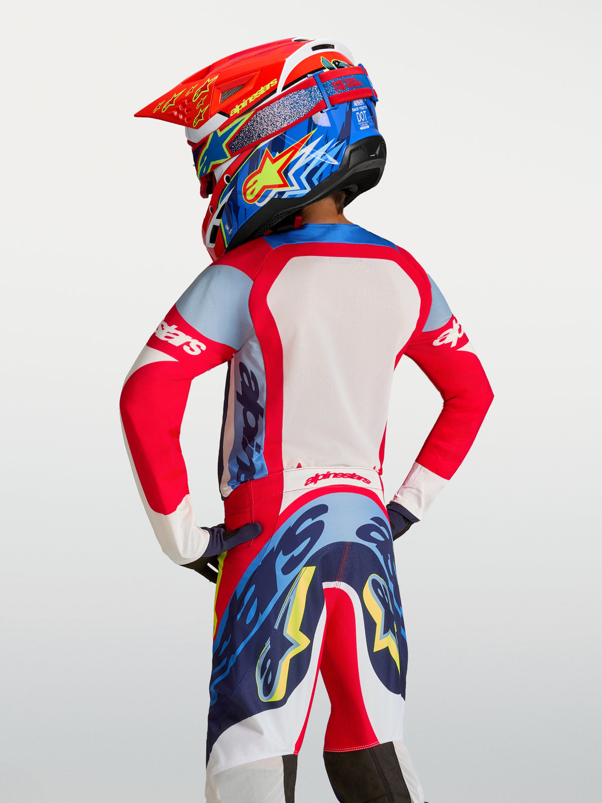 Alpinestars Camisola Supertech Dyna Jovem 2027, camisola de motocross para corrida, vermelha e azul-marinho, malha respirável, vista traseira no piloto.