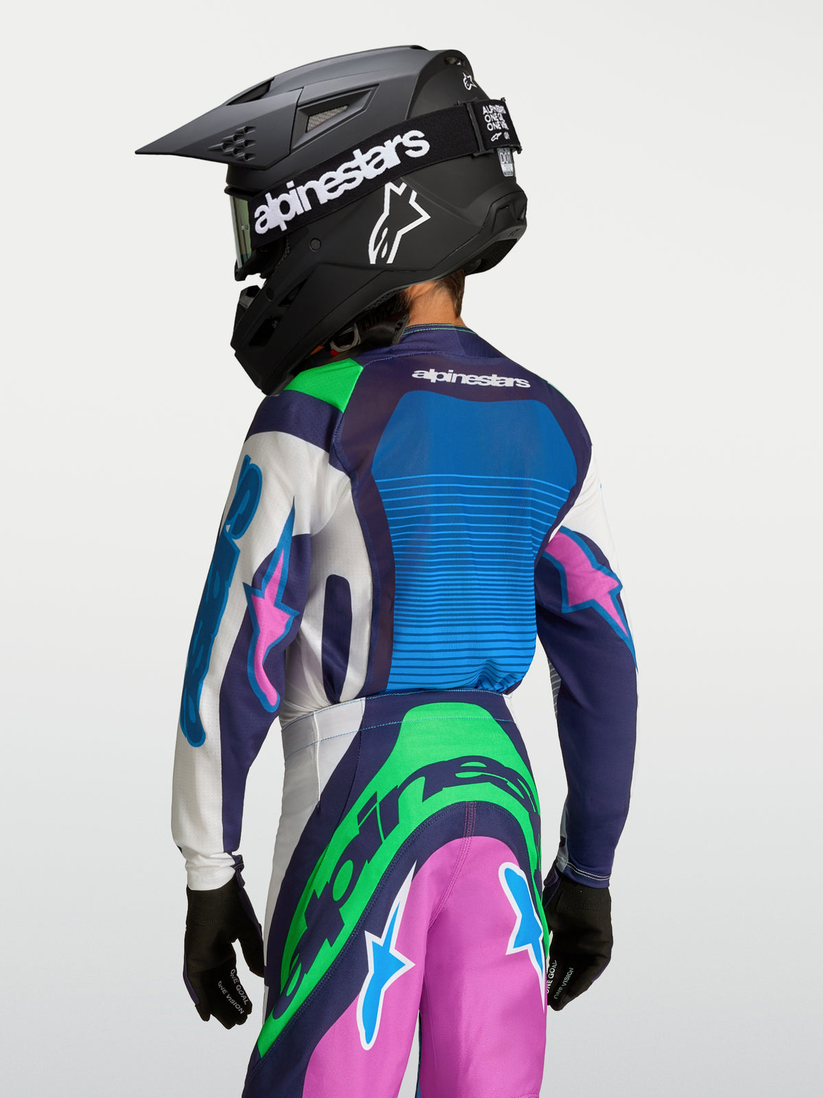 Alpinestars Supertech Maven Jovem, camisola de motocross azul e verde, vista traseira com capacete.