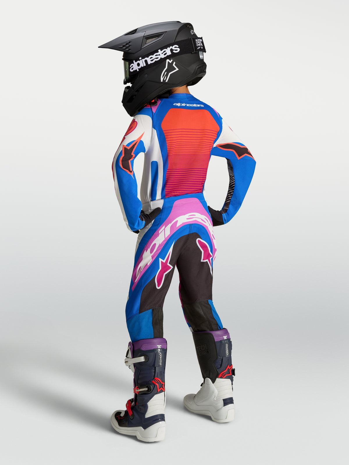 Alpinestars 2027 Juventude Supertech Maven Gear Set, conjunto de motocross azul e laranja coral, vista traseira num jovem piloto.