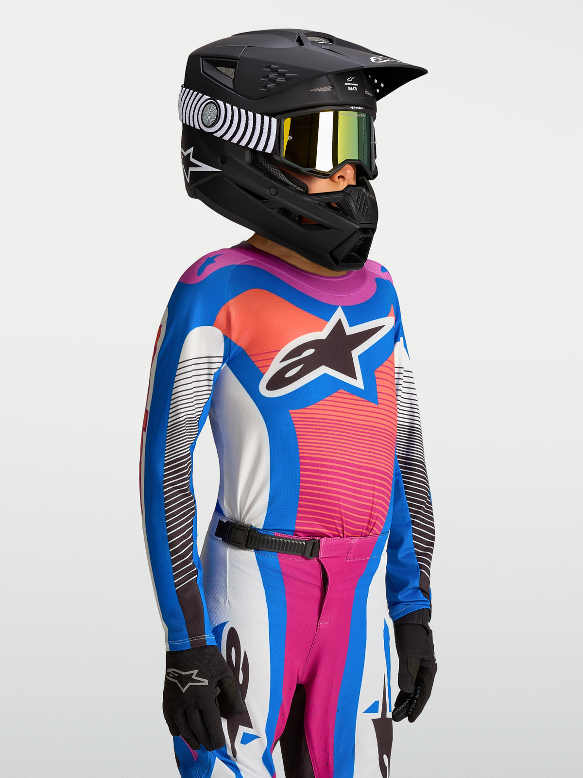 Alpinestars Youth Supertech Maven Jersey, blue and coral breathable motocross gear for youth with a black racing helmet.