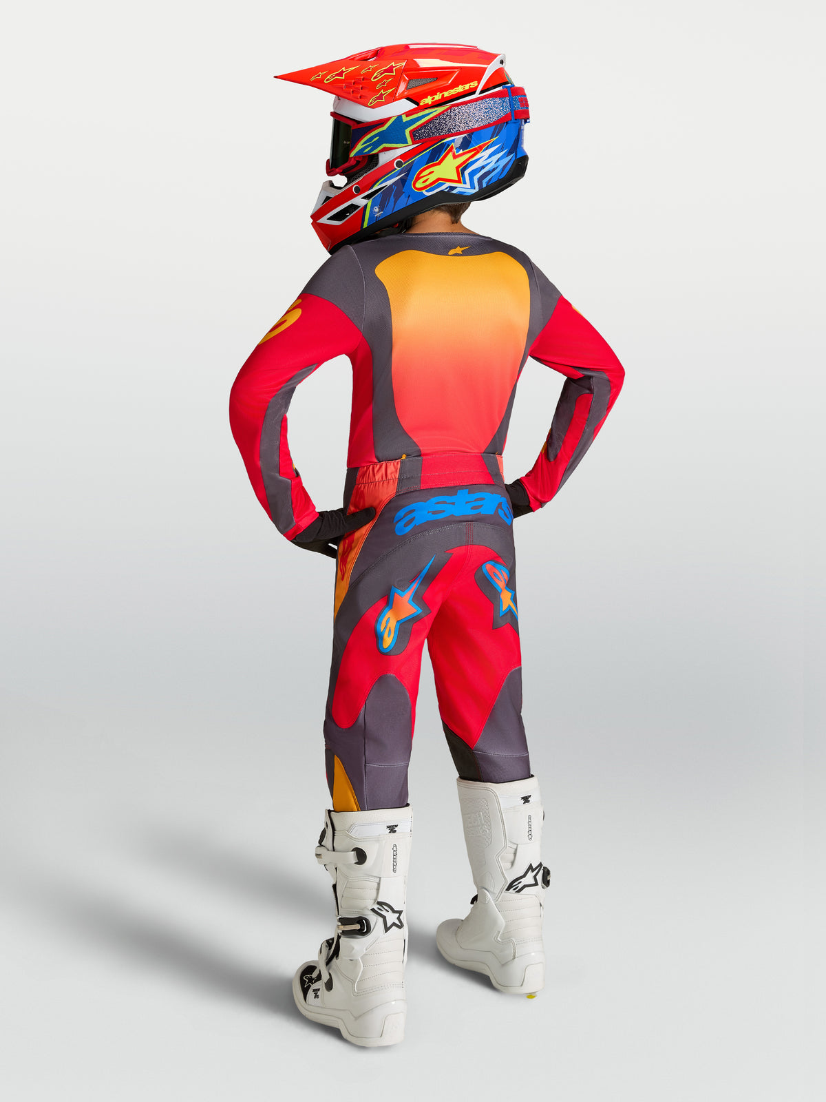 Alpinestars Juventude Fluid Hunt Gear Set, conjunto de motocross vermelho e cinzento com botas brancas, vista traseira.