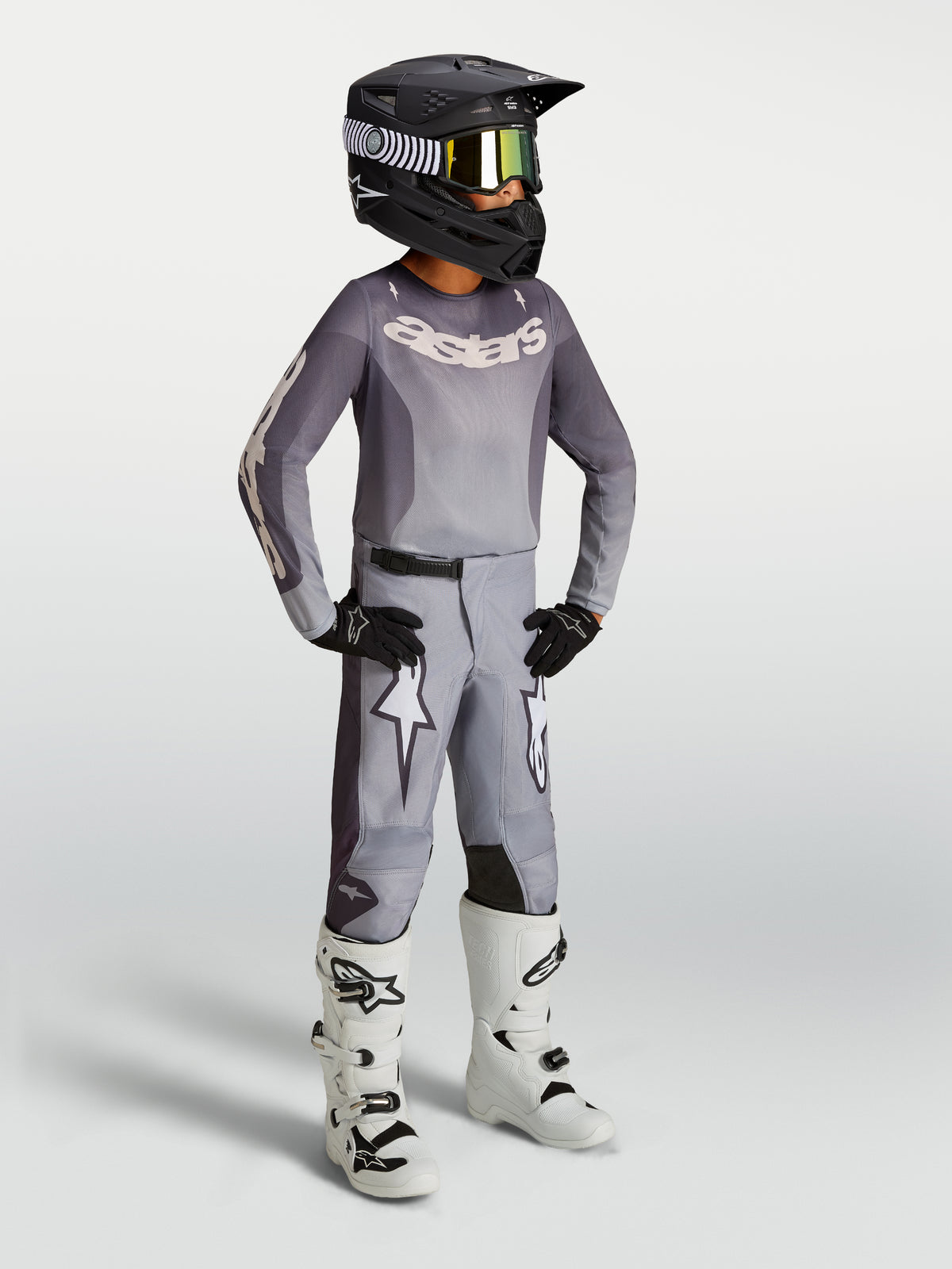 Alpinestars Juventude Fluid Amber Gear Set, conjunto de motocross cinzento com botas brancas e capacete preto.