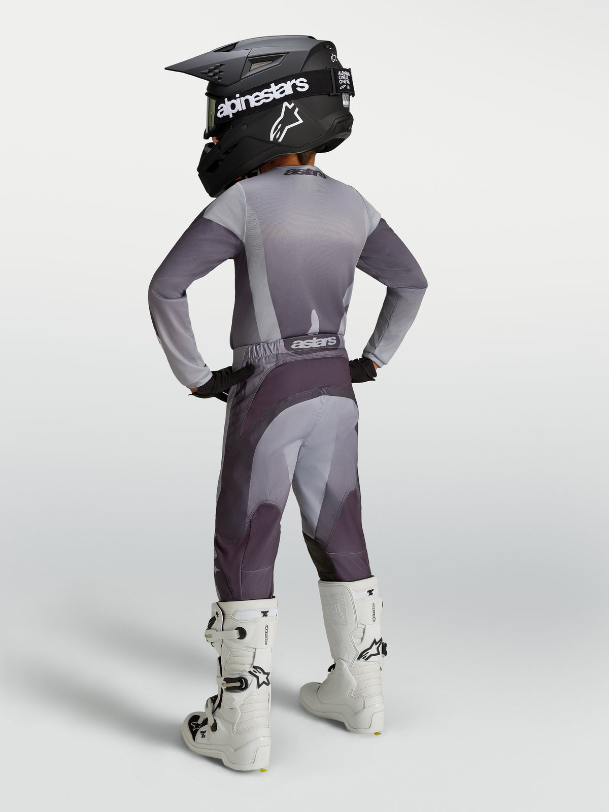 Alpinestars 2027 Juventude Fluid Amber Gear Set, conjunto cinzento e roxo, vista traseira com capacete e botas brancas.