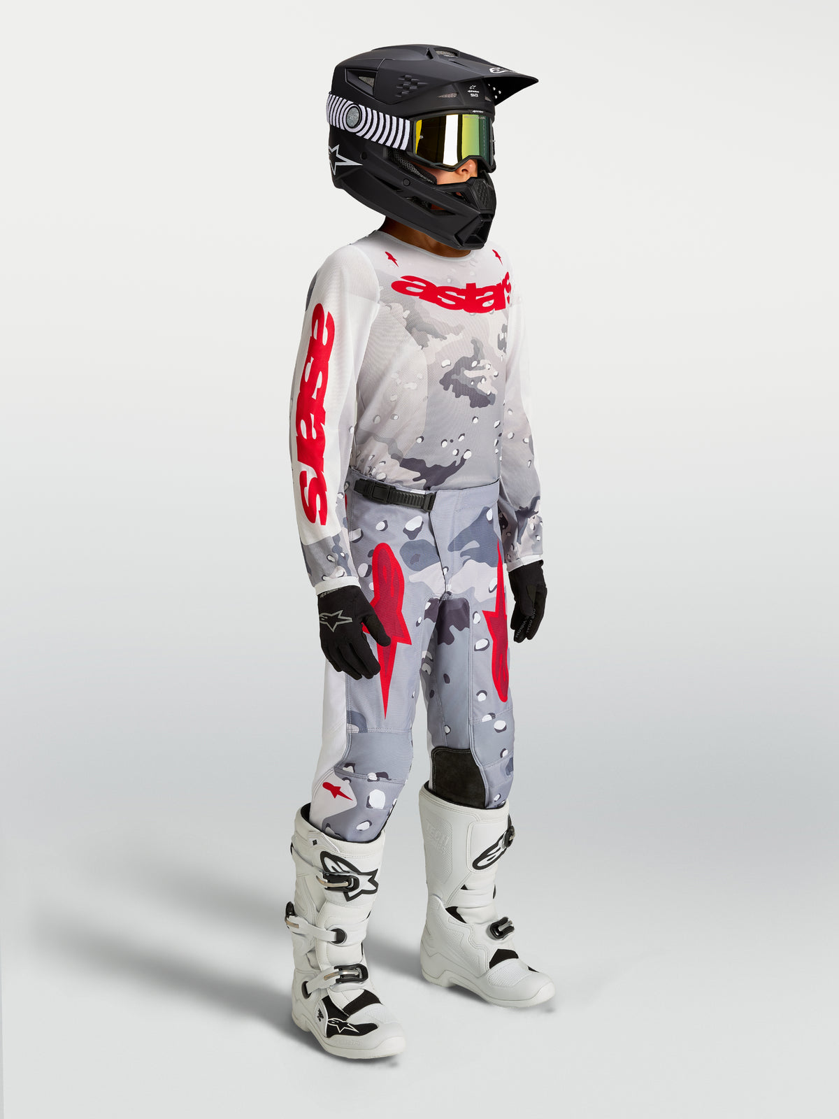 Alpinestars Juventude Fluid Lone Gear Set, conjunto de motocross cinzento camuflado e vermelho, piloto com botas brancas.