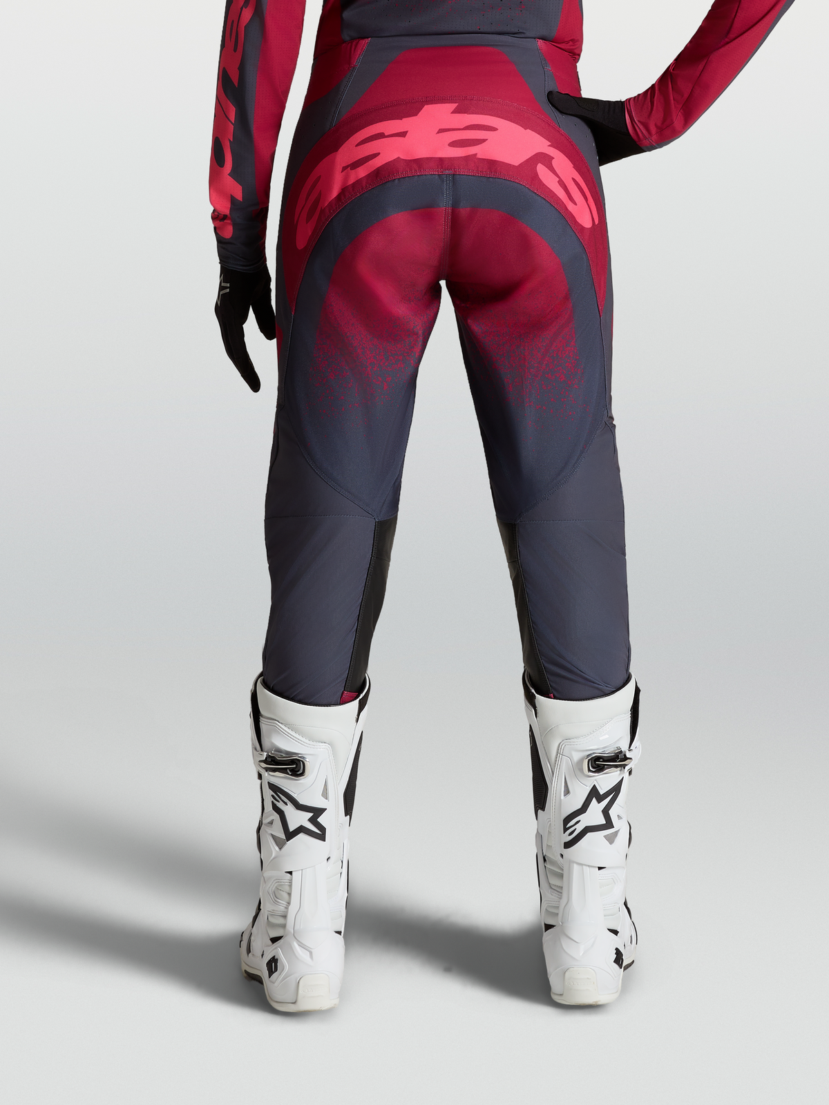 Alpinestars Calças Stella Techstar Swan, equipamento de motocross para mulher, vermelho e cinzento, vista traseira com botas de corrida brancas.