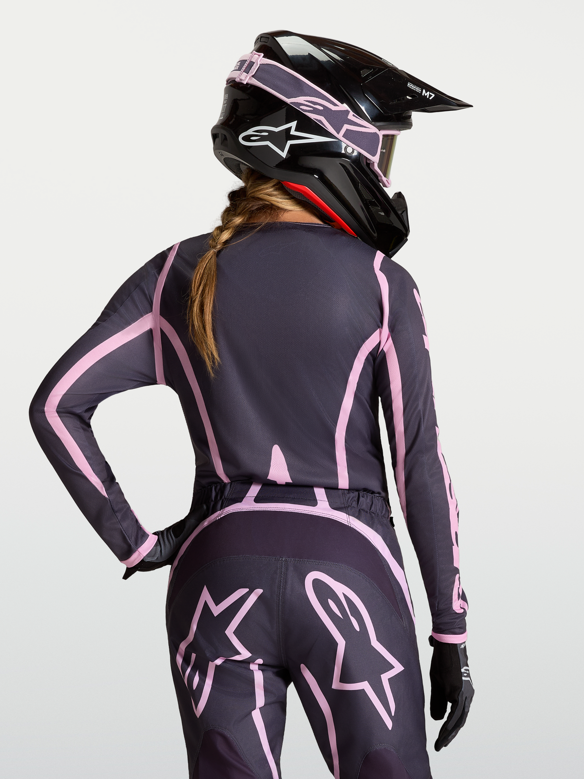 Alpinestars Camisola Stella Fluid Apex V2, camisola de motocross para mulher, cinzenta e rosa, vista traseira, com capacete a condizer.