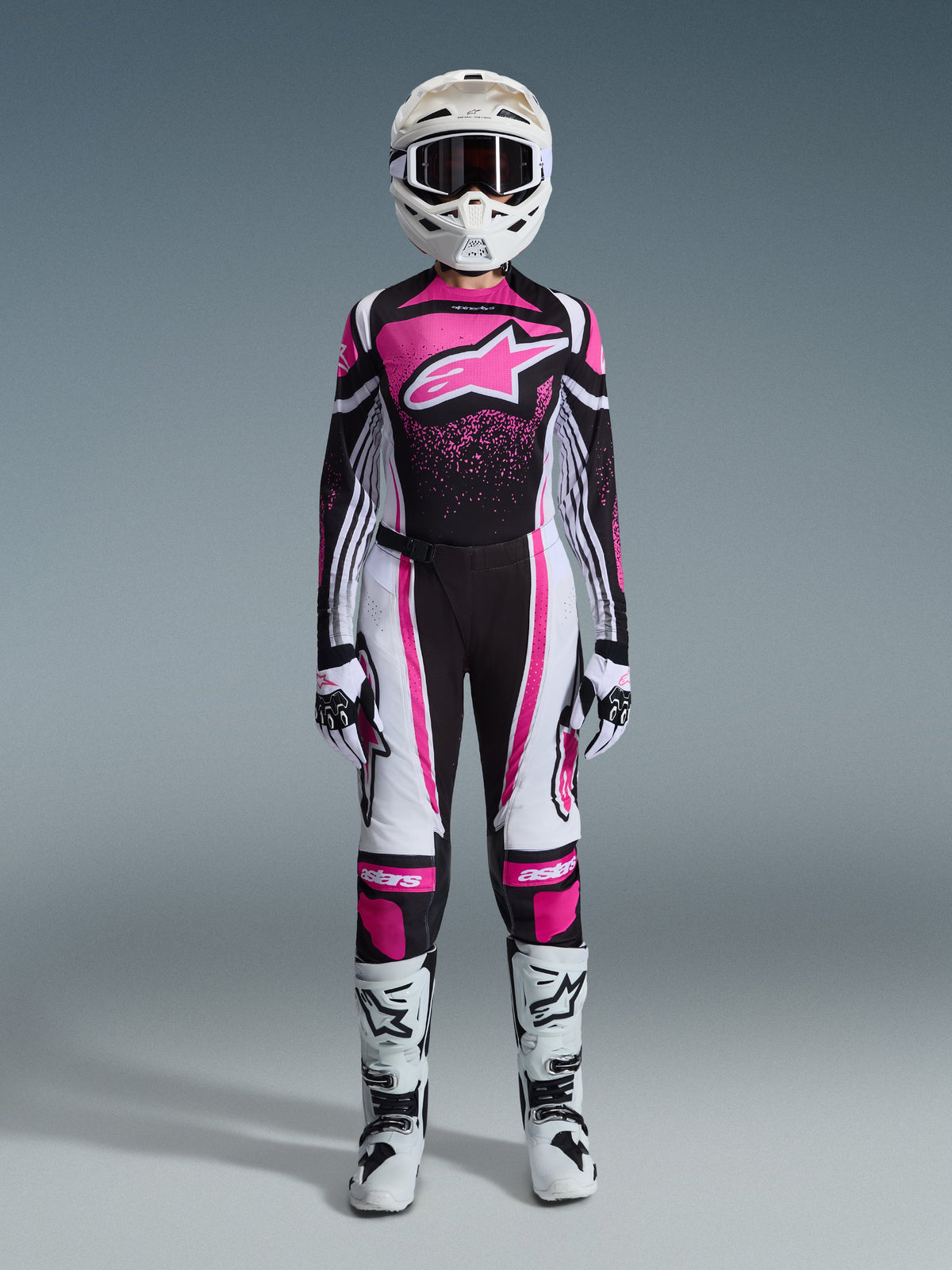 Conjunto de equipamento Alpinestars Stella Techstar Nomur 2026 para mulher, fato completo de motocross em preto, branco e fúcsia, camisola com logótipo de estrela grande e design de salpicos cor-de-rosa, calças a condizer, capacete branco com óculos, botas pretas e brancas, equipamento de todo-o-terreno coordenado para mulher