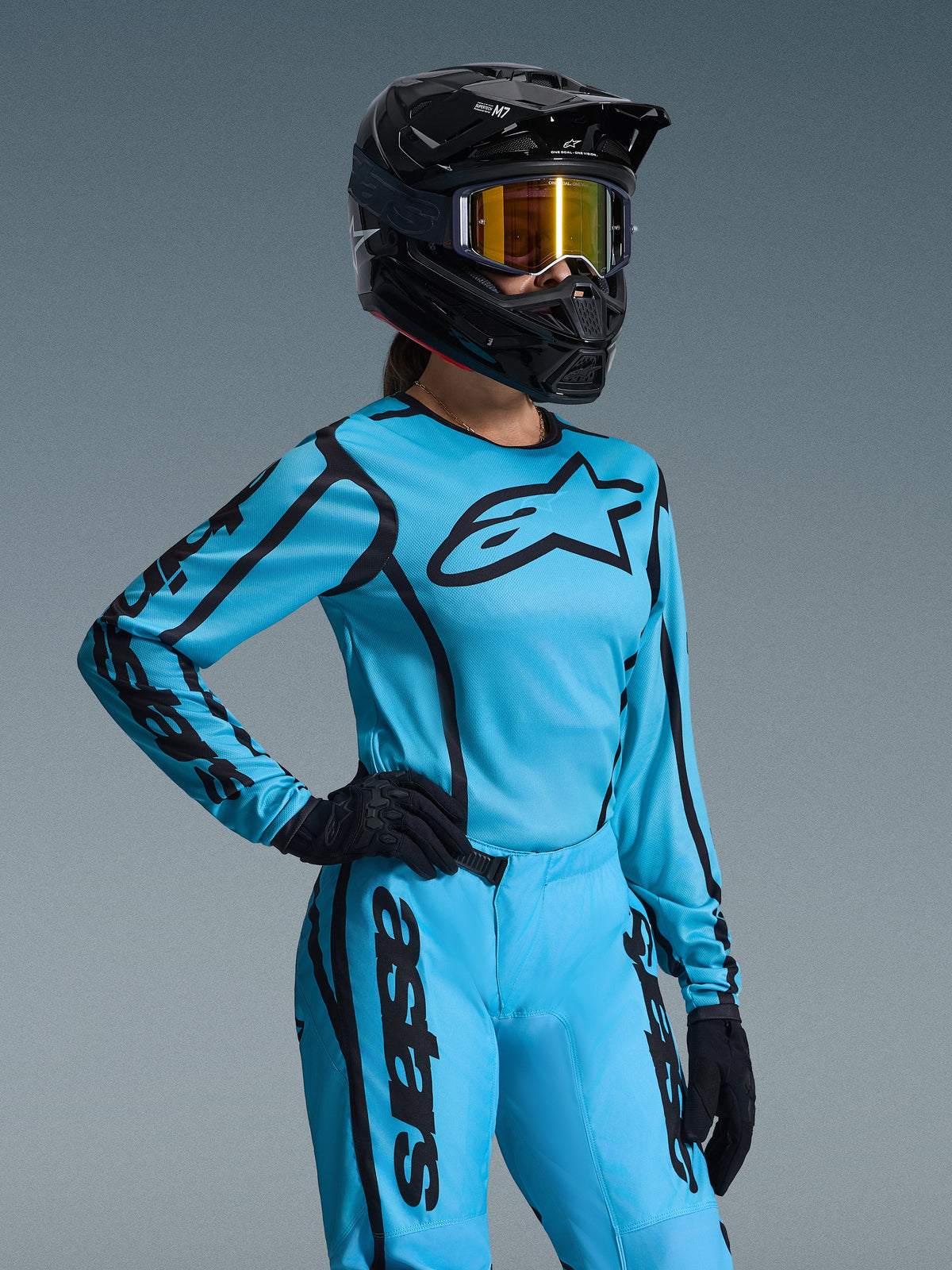 Conjunto de Equipamento Alpinestars Stella Fluid Apex 2026 para Mulher, azul brilhante e preto, camisola e calças de motocross com logótipos pretos, usado com capacete preto, óculos com lente espelhada dourada e luvas pretas, corte feminino específico para corridas off-road