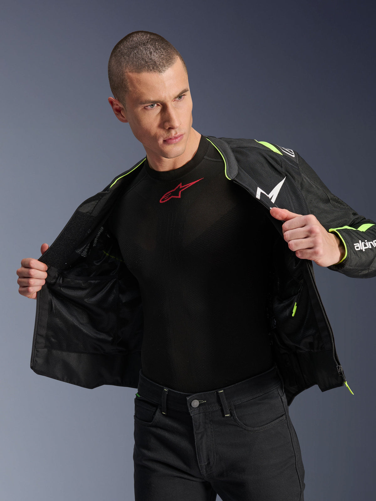 Modelo masculino a usar o casaco Alpinestars T-Sps Air V2 em preto e amarelo fluo, aberto para destacar a construção interna em malha e os bolsos, combinado com uma camada base preta Alpinestars e calças pretas, num estilo de equipamento de condução urbana para motociclistas.