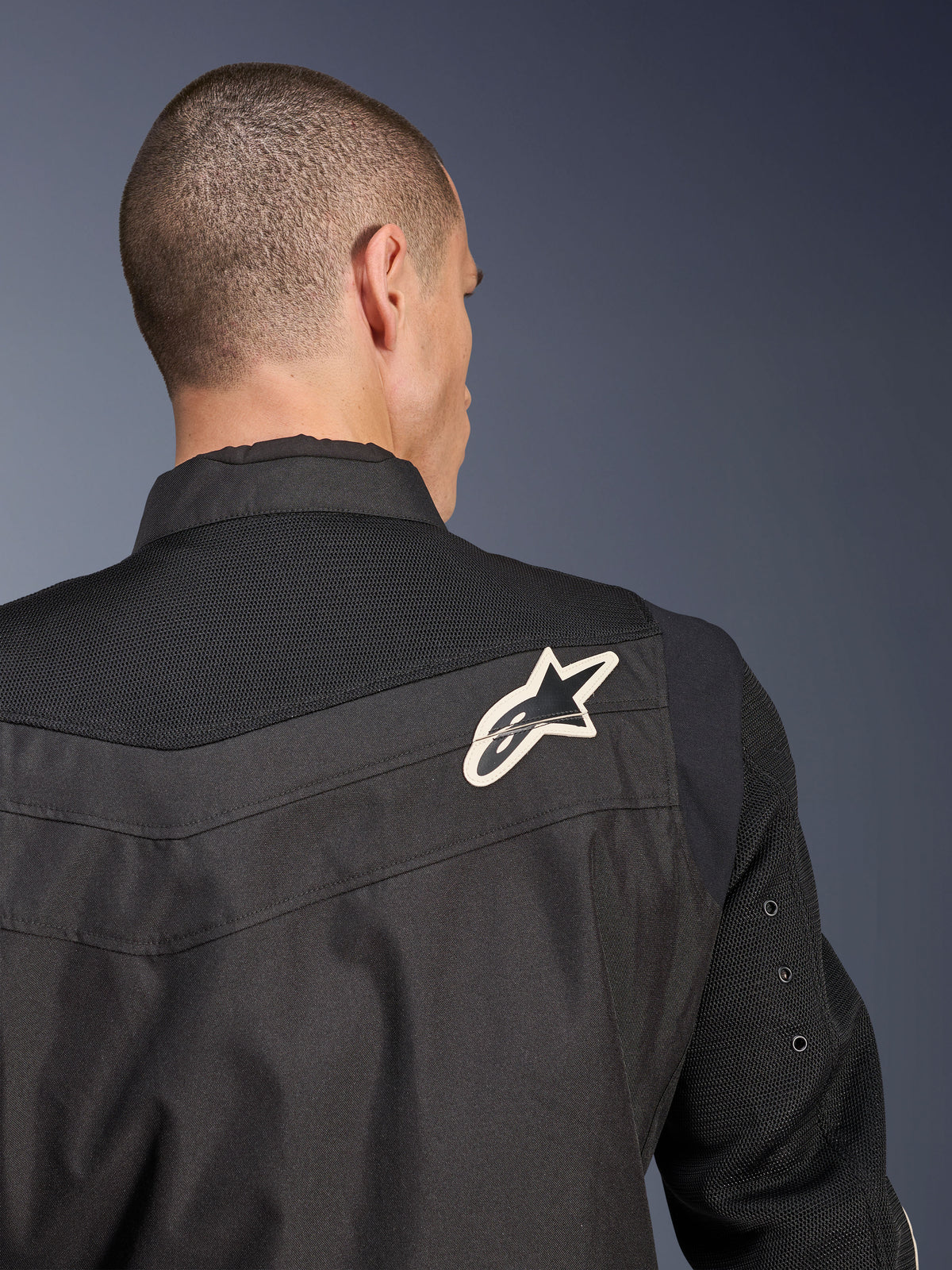 Alpinestars T-Dyno Air Jacket, casaco de motociclismo em têxtil preto, vista de trás em pormenor realçando a zona dos ombros e as mangas em malha 3D respirável, com logótipo de estrela branco e preto no ombro direito.
