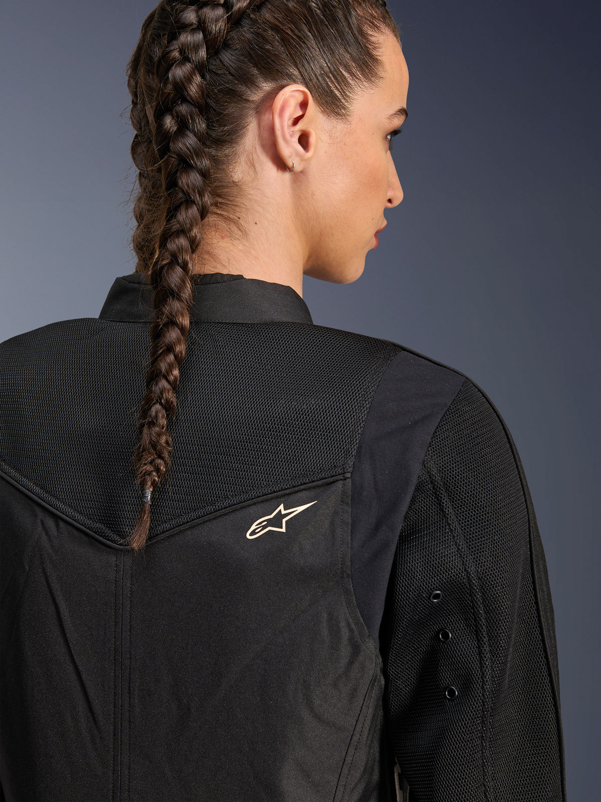 Alpinestars Stella T-Dyno Air Jacket, casaco de motociclismo feminino preto, vista aproximada das costas mostrando painéis de malha 3D na pala e parte superior das costas para ventilação, pequeno logótipo de estrela branco, modelo com cabelo entrançado