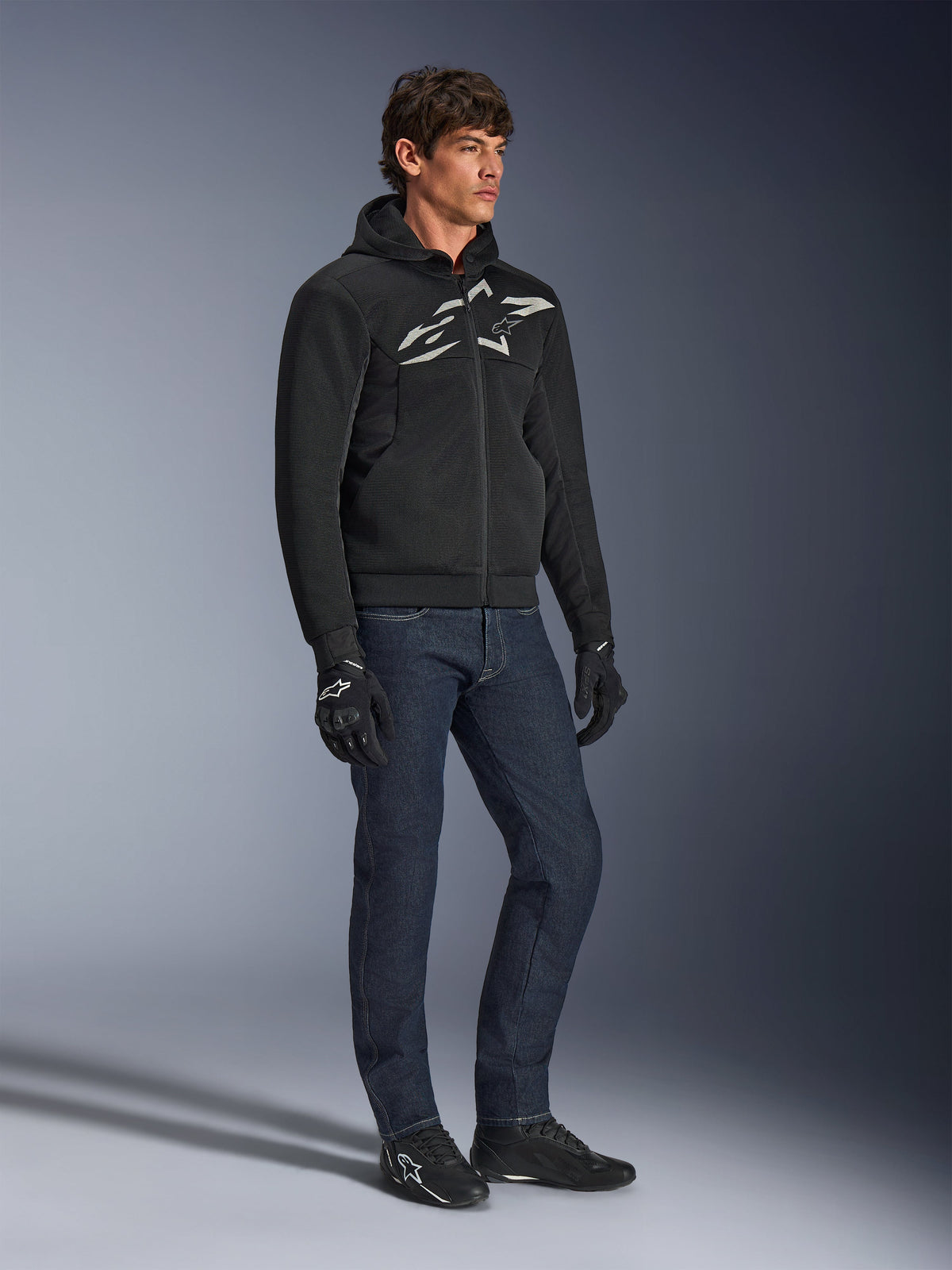 Alpinestars Chrome Superairflow Hoodie, black with white and gray logo, 3D mesh ventilated textile construction, worn with dark blue denim jeans and black motorcycle gloves, urban sport riding style.