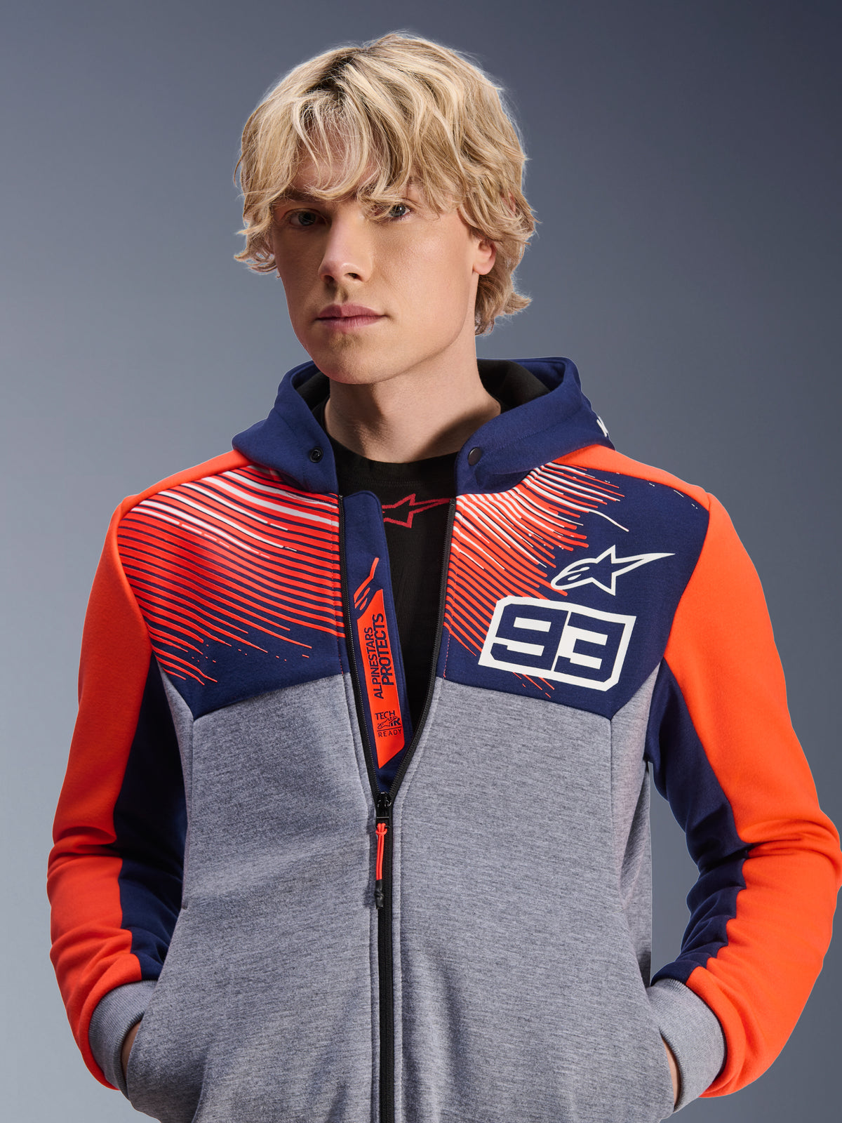 Alpinestars MM93 Chrome V2 Sport Hoodie, hoodie de motociclismo urbano, azul-marinho e cinza mesclado com detalhes em vermelho fluorescente, com a marca Marc Márquez 93 e o logótipo Alpinestars, design com fecho integral, vestuário casual para motociclistas