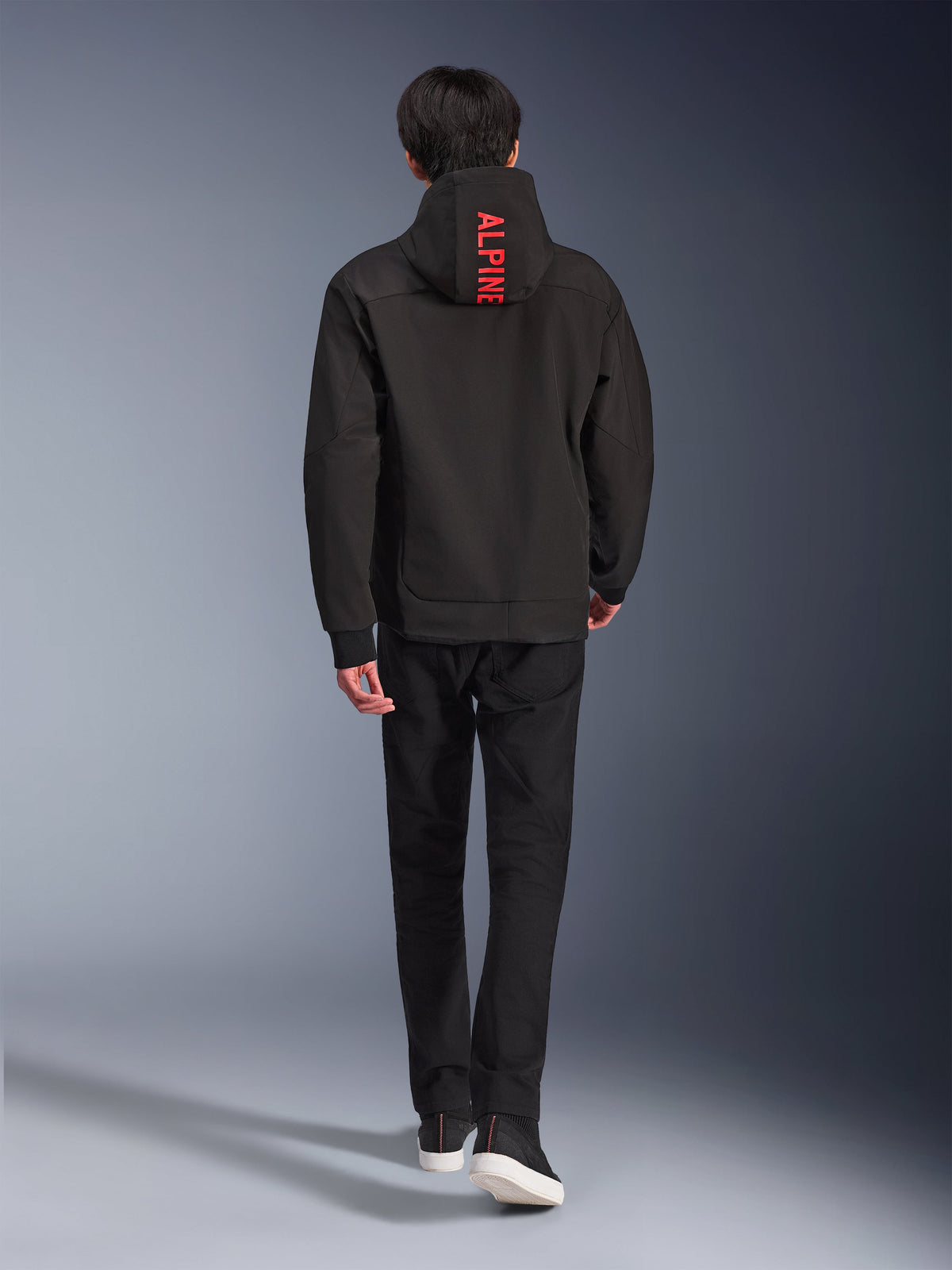 Alpinestars Radium Tech Hoodie, urban motorcycle jacket, Black, back view featuring bright red 'ALPINE' text on the hood, worn with black pants and sneakers, sleek technical shell for commuting.