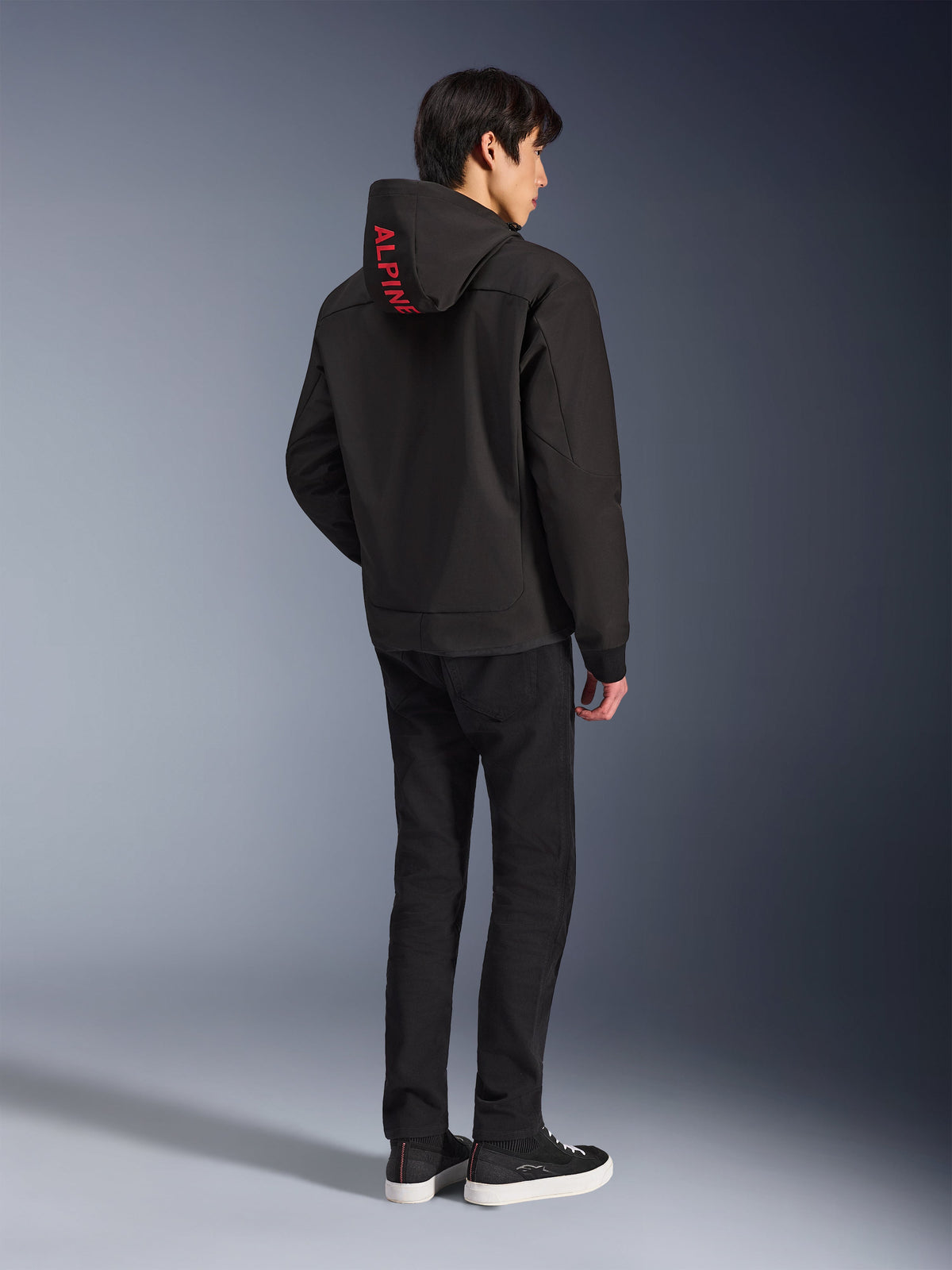 Alpinestars Radium Tech Hoodie, Black with red Alpinestars branding on the hood, back view on a male model, worn with black pants and sneakers, technical urban riding gear