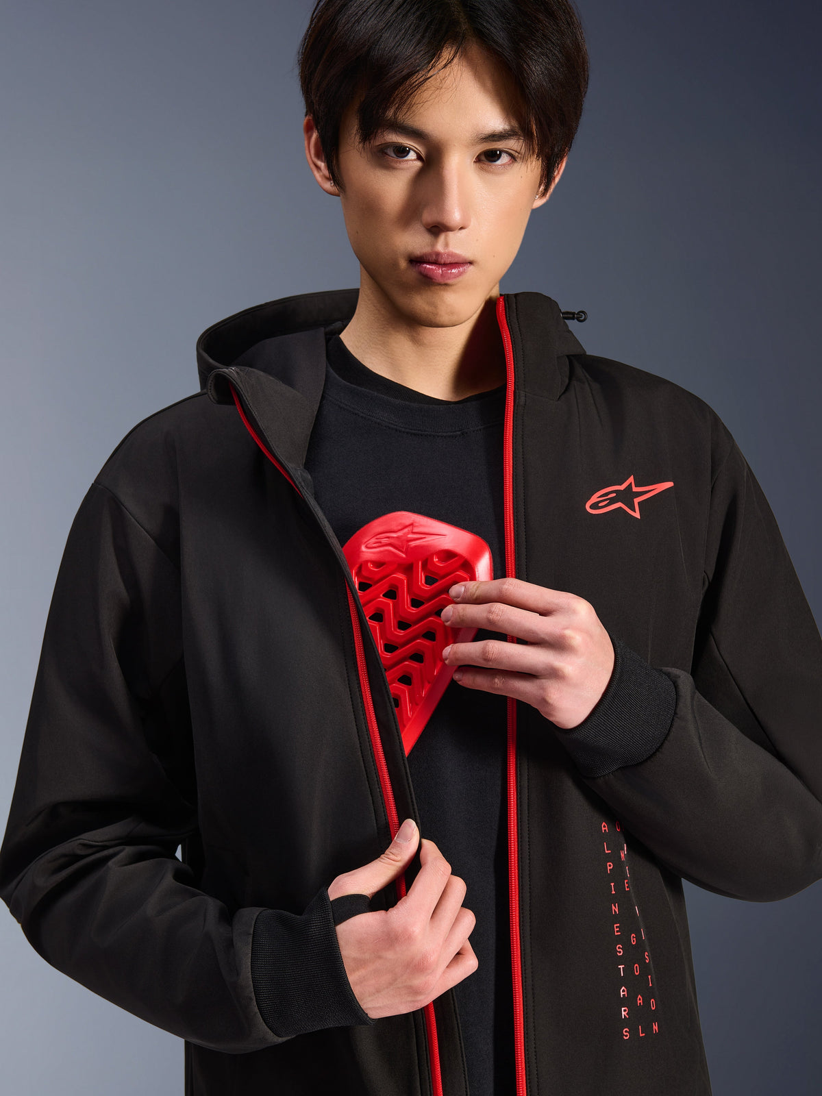 Alpinestars Radium Tech Hoodie, Urban Motorcycle Jacket, Black and Bright Red, worn by a model showing a red chest armor insert, features bright red zippers and vertical Alpinestars branding, sleek windproof technical shell for urban commuting