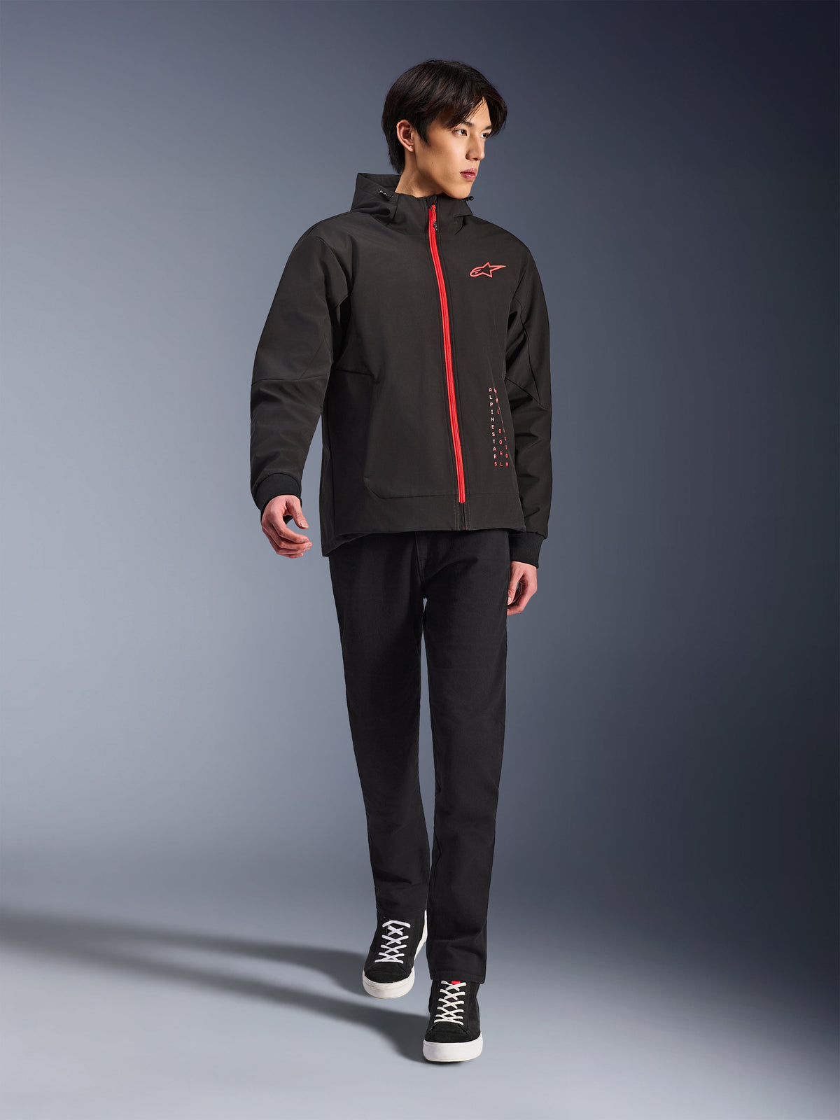 Alpinestars Radium Tech Hoodie in Black Bright Red, urban motorcycle jacket worn by a model, featuring a red front zipper and chest logo, styled with black pants and sneakers for a modern commuting look.
