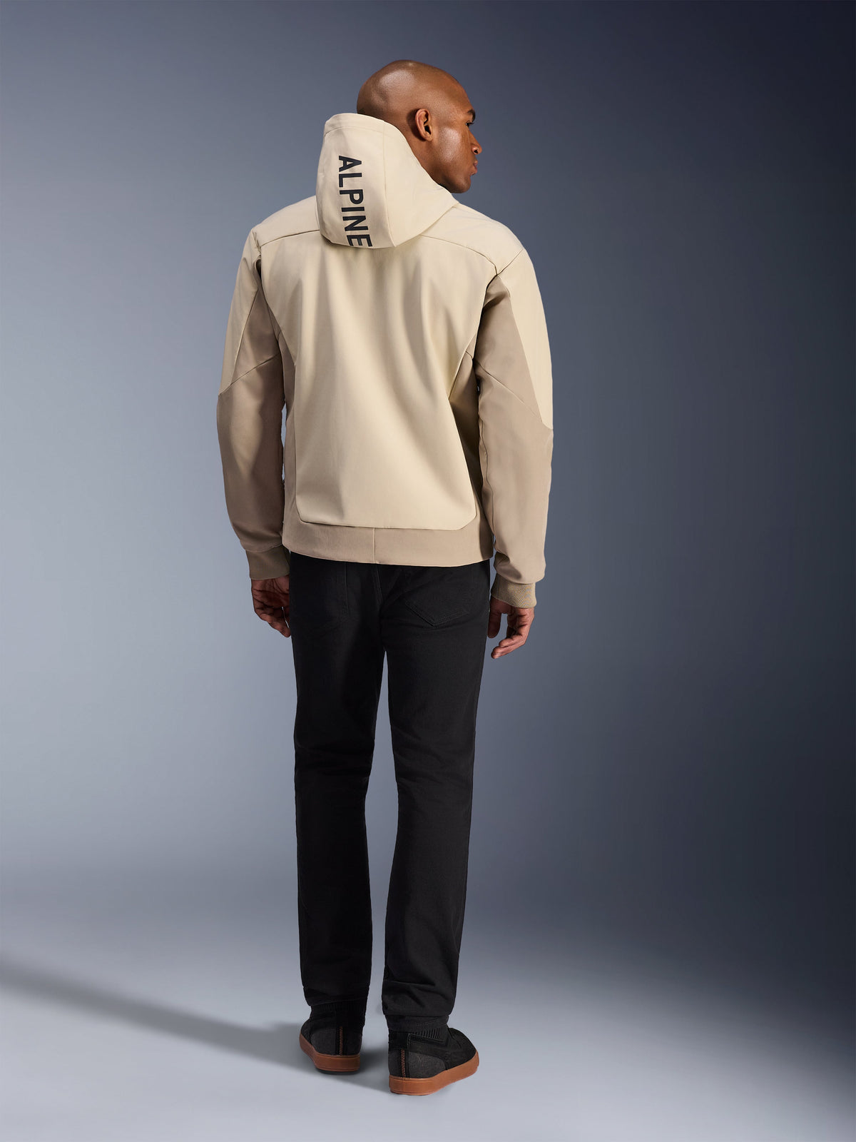 Alpinestars Radium Tech Hoodie, Mastic Aluminum, vista traseira a mostrar o texto vertical 'ALPINE' no capuz, casaco de motociclismo urbano com casco técnico 3L à prova de vento e painéis beges, usado com calças pretas
