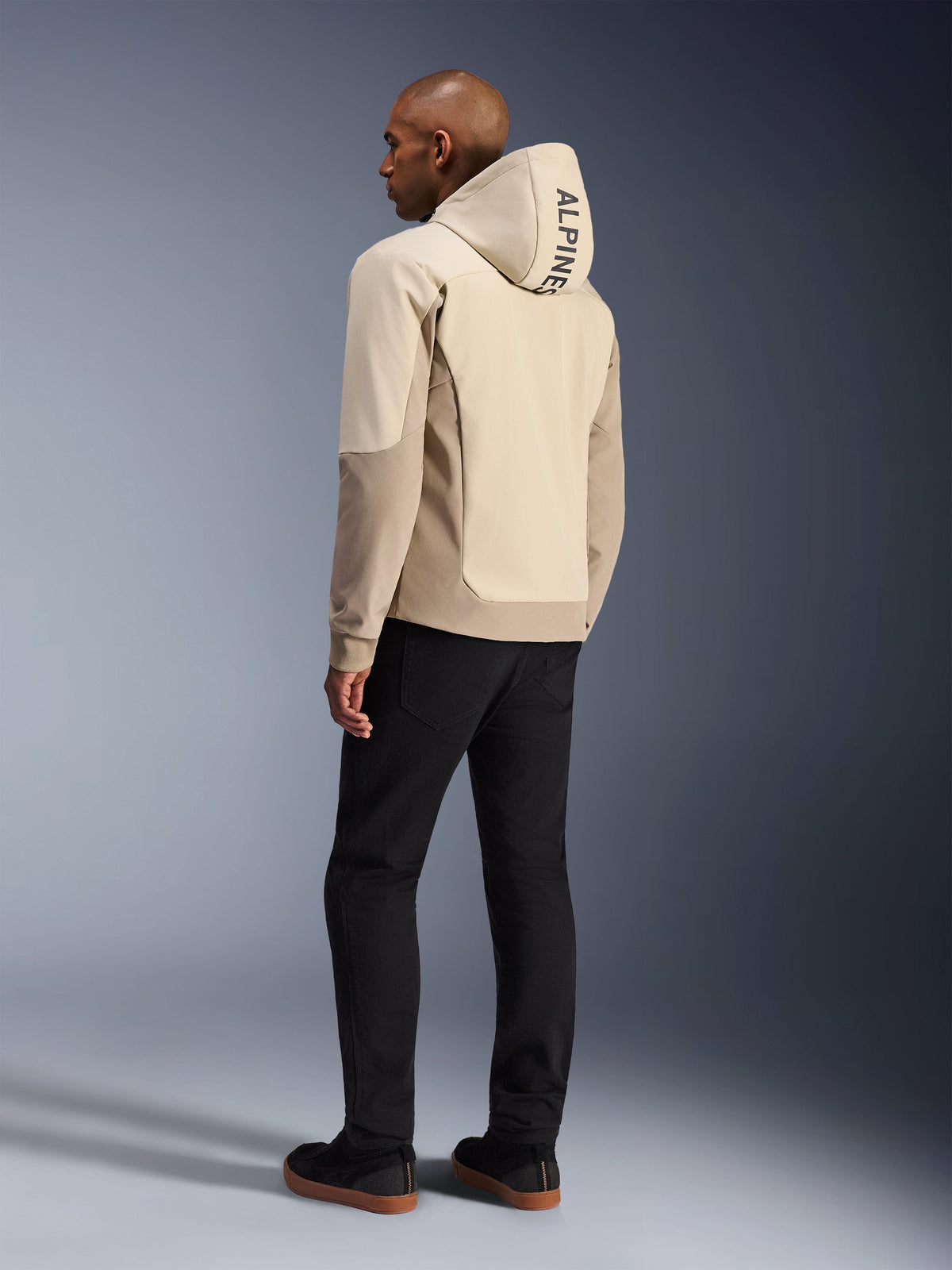 Alpinestars Radium Tech Hoodie em Mastic Aluminum, casaco de motociclismo urbano, vista traseira num modelo com o capuz levantado, logótipo vertical ALPINESTARS no capuz, combinado com calças pretas, construção têxtil moderna para proteção na condução urbana
