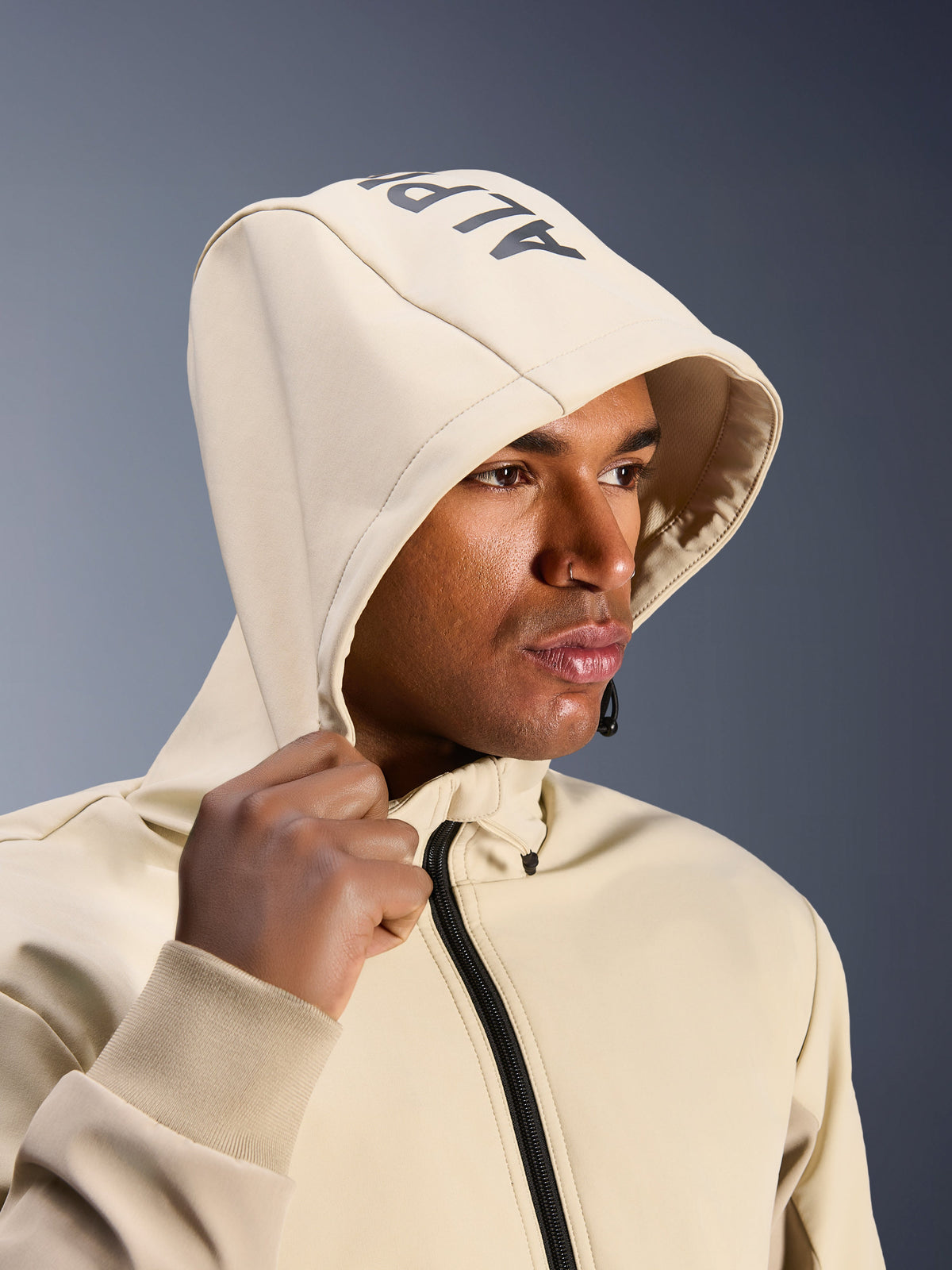 Alpinestars Radium Tech Hoodie em Mastic Aluminum, grande plano de um homem com o capuz colocado, apresentando a marca Alpinestars no topo, casaco de motociclismo urbano com camada técnica corta-vento, estética streetwear moderna para condução urbana