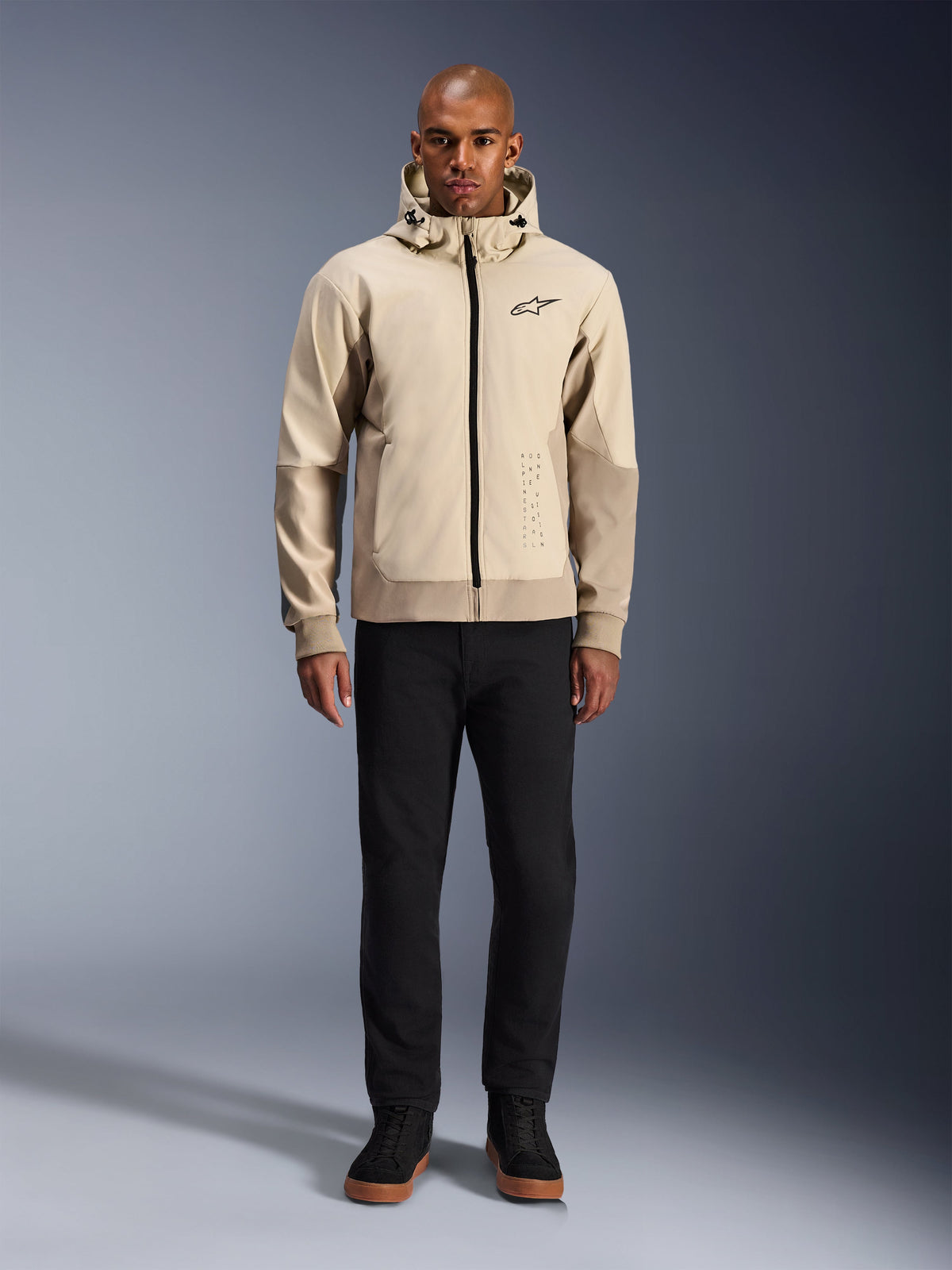 Alpinestars Radium Tech Hoodie em Mastic Aluminum, hoodie de motociclismo urbano usado por um modelo masculino com calças pretas e botas pretas, com fecho de correr integral preto, pequeno logótipo no peito e corte atlético para condução urbana.