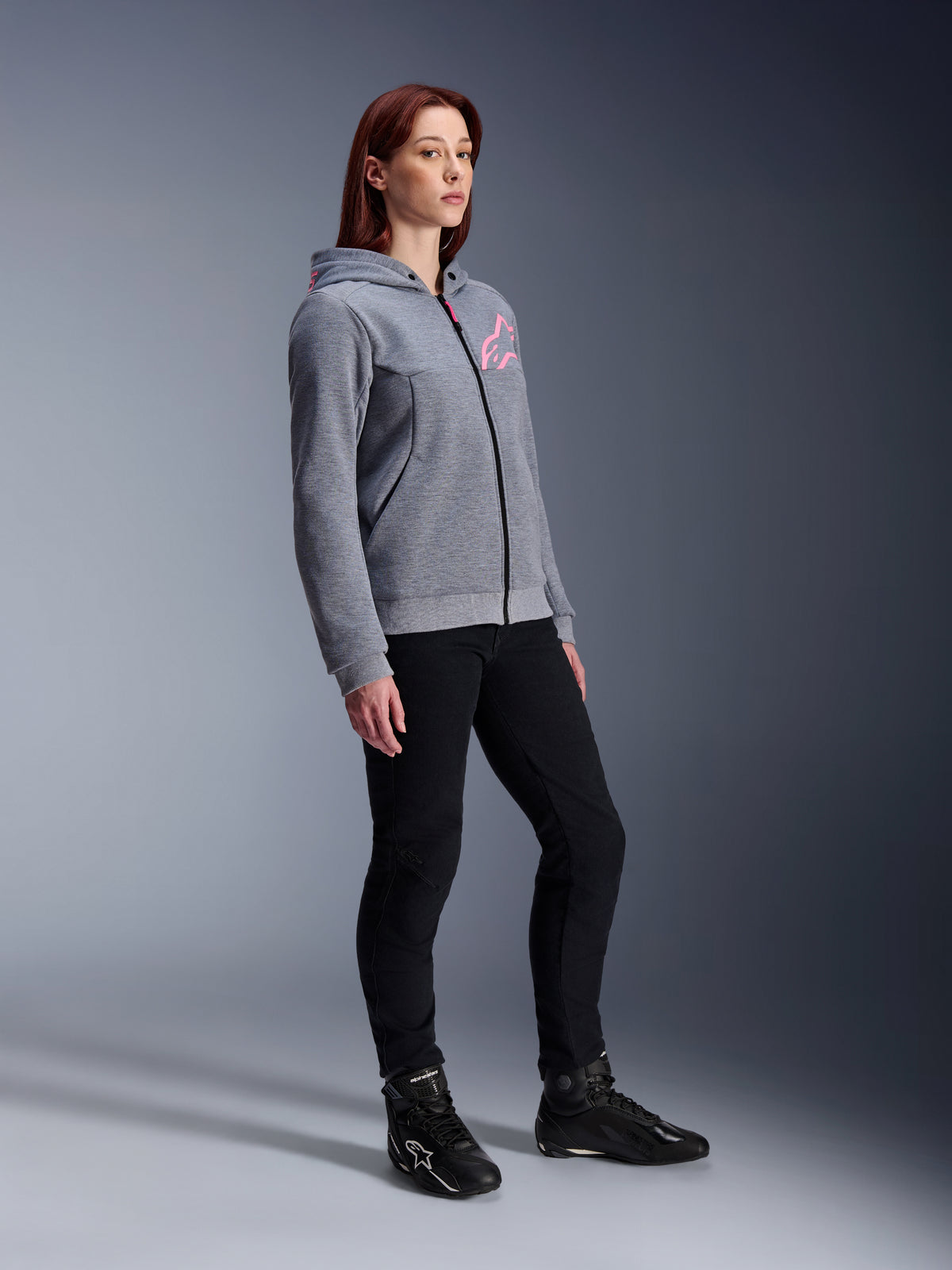 Alpinestars Stella Chrome V2 Sport Hoodie, hoodie de motociclismo para mulher, cinza mesclado e rosa fluo, usado com calças de condução pretas e botas pretas, equipamento de condução urbana casual