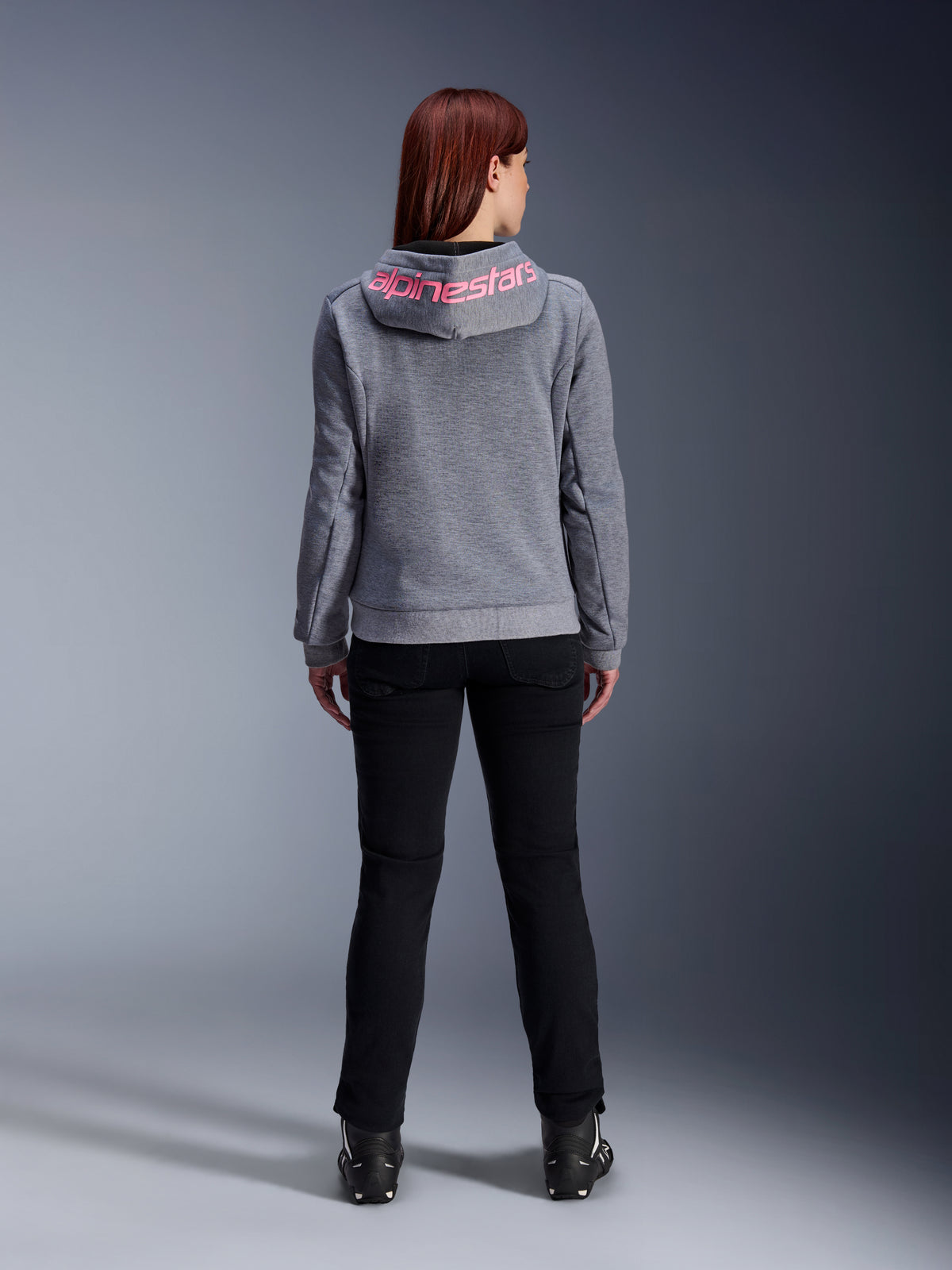 Alpinestars Stella Chrome V2 Sport Hoodie, hoodie de motociclismo para mulher, cinzento mesclado e rosa fluo, vista traseira com o logótipo Alpinestars rosa no capuz, usado com calças e botas pretas, vestuário casual de motociclismo para mulher