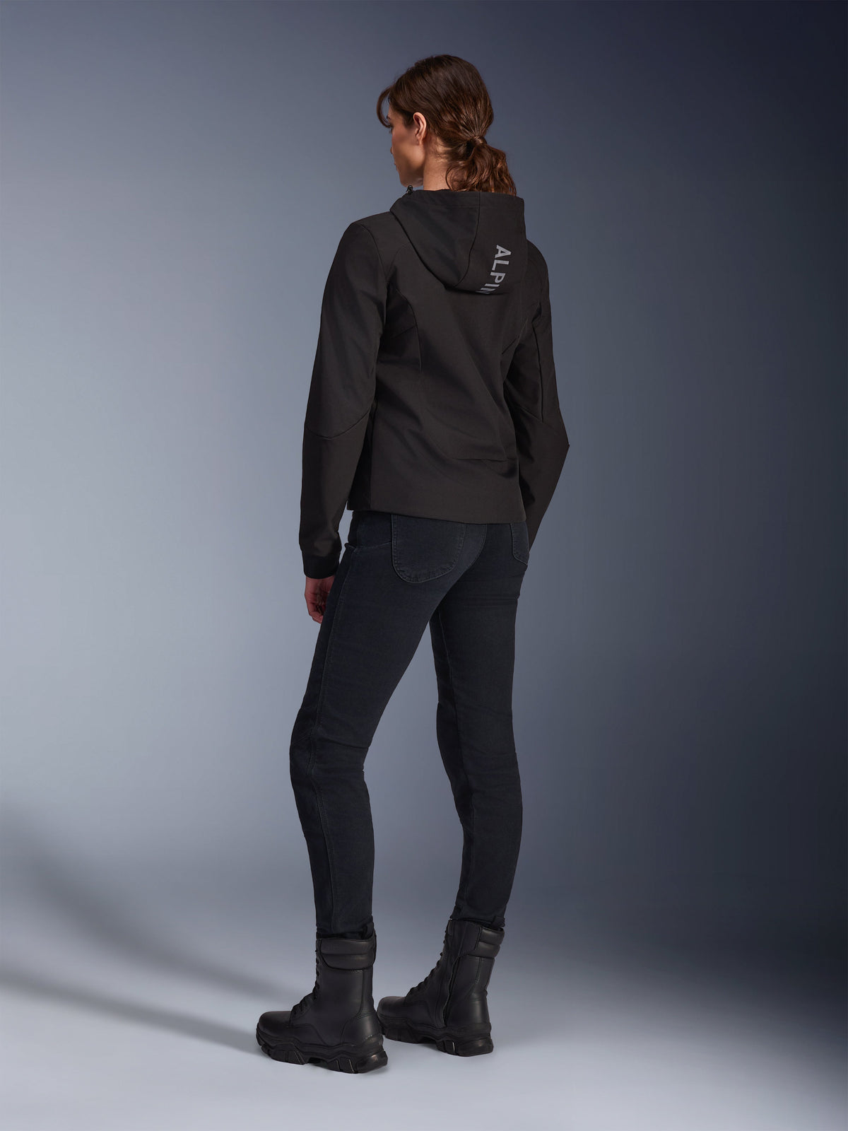 Alpinestars Stella Radium Tech Hoodie, hoodie de condução urbana preto para mulher, vista traseira mostrando a marca 'ALPIN' no capuz, combinado com calças técnicas de condução pretas e botas pretas, estrutura técnica leve e corta-vento.