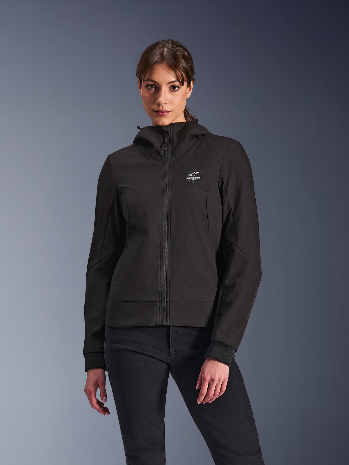 Alpinestars Stella Radium Tech Hoodie, casaco de motociclismo com capuz para mulher, preto, design com fecho, logótipo circular no peito e capuz, vestuário técnico de condução urbana, usado por modelo