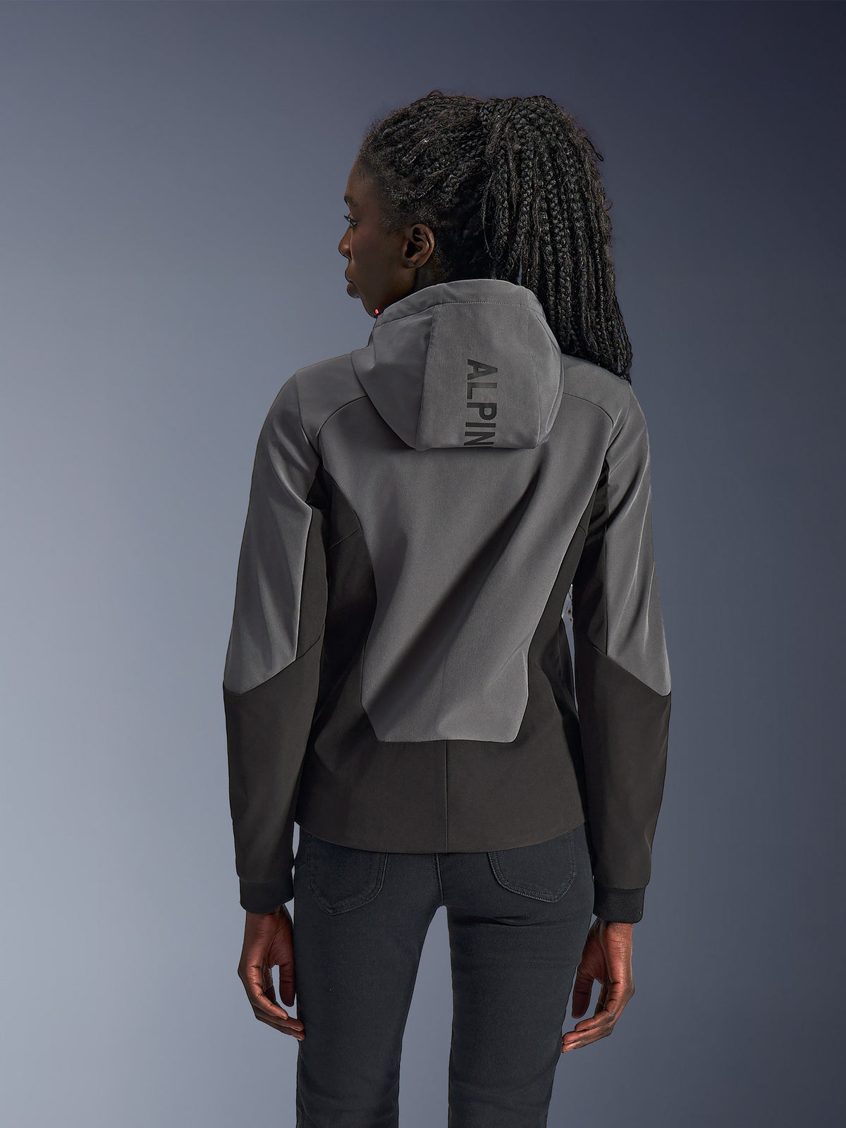 Woman wearing Alpinestars Stella Radium Tech Hoodie, rear view, Deep Gray Black, two-tone gray and black 3-layer windproof shell, Alpinestars branding on the hood, athletic fit urban motorcycle apparel