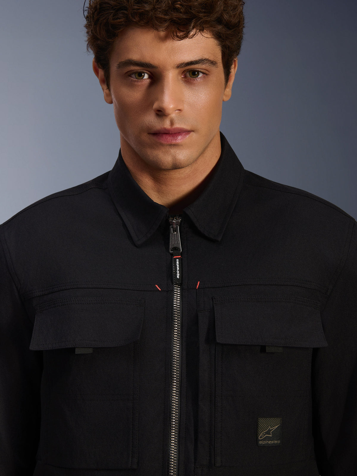 Alpinestars Bryon Water Resistant Overshirt, preto, vista em pormenor do fecho de correr frontal e bolsos no peito, textura de lona encerada durável, design urbano minimalista com pormenores da marca e etiqueta com logótipo tecido