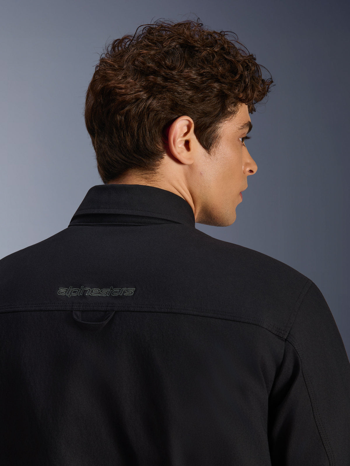 Alpinestars Bryon Water Resistant Overshirt, casaco de motociclismo urbano, preto, grande plano da zona posterior dos ombros com logótipo bordado e presilha, construção em lona encerada resistente à água.