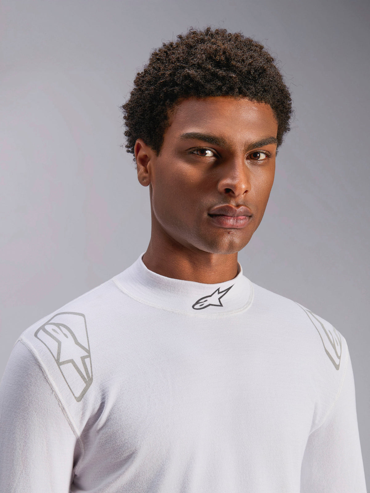 Alpinestars ZX Evo V3 Top - Manga Comprida, camada de base branca para automobilismo, vestido por um modelo masculino, gola subida com logótipo Alpinestars preto, grafismos prateados nos ombros, roupa interior de desporto motorizado leve e resistente a chamas