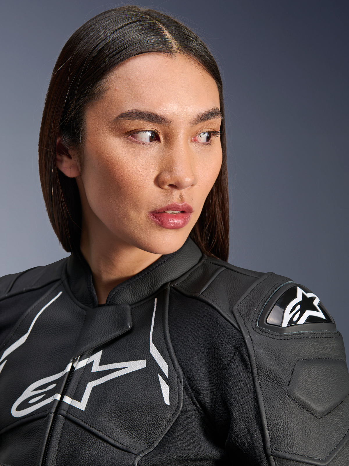 Mulher a usar o Casaco de Couro Stella Dusk da Alpinestars em preto e branco, retrato em grande plano com o logótipo Alpinestars branco no peito e protetor de ombro externo DFS, construção em couro premium para motociclismo de estrada