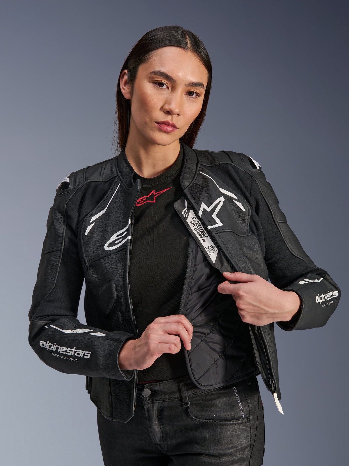 Modelo feminina a usar o Casaco de Couro Alpinestars Stella Dusk em Preto e Branco, destacando o forro térmico acolchoado interno e a etiqueta Tech-Air Ready, couro bovino premium com logótipo de estrela branca e marcação 'RACING AHEAD' na manga