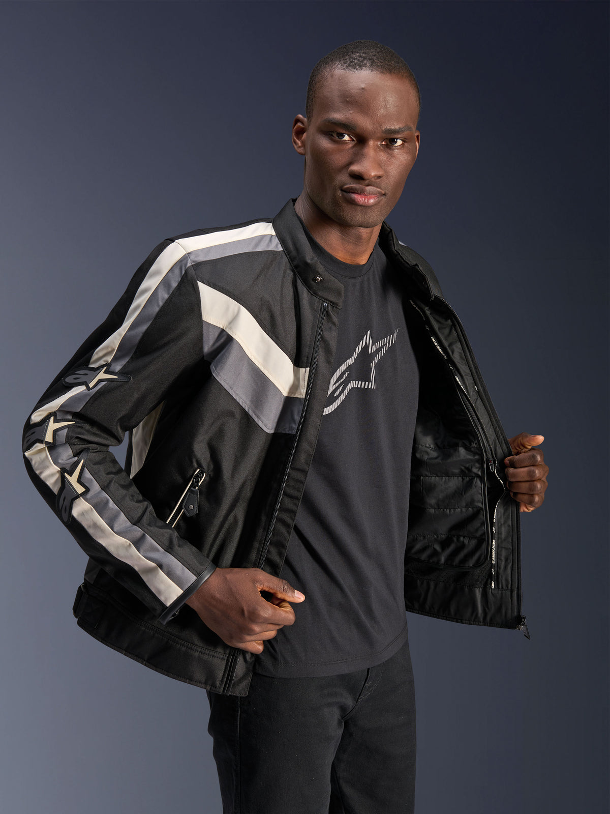 Casaco Alpinestars T-Dyno WR, Preto, Cinzento Escuro e Ecru, casaco de motociclismo têxtil com corte de motociclista de inspiração vintage, detalhes de riscas no peito e nas mangas, vestido sobre uma t-shirt gráfica preta, equipamento de condução urbana