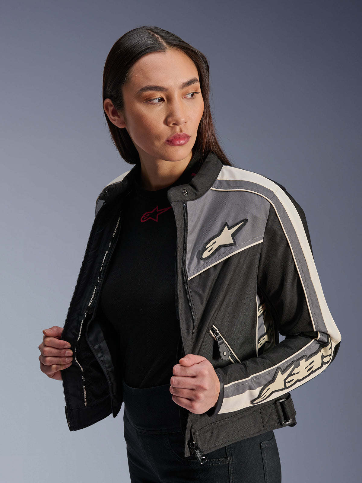 Casaco Alpinestars Stella T-Dyno WR para mulher, casaco de motociclismo têxtil, preto, cinzento escuro e cru, design de inspiração vintage com riscas desportivas e logótipos no peito e mangas, vestido por uma modelo, equipamento de condução urbana