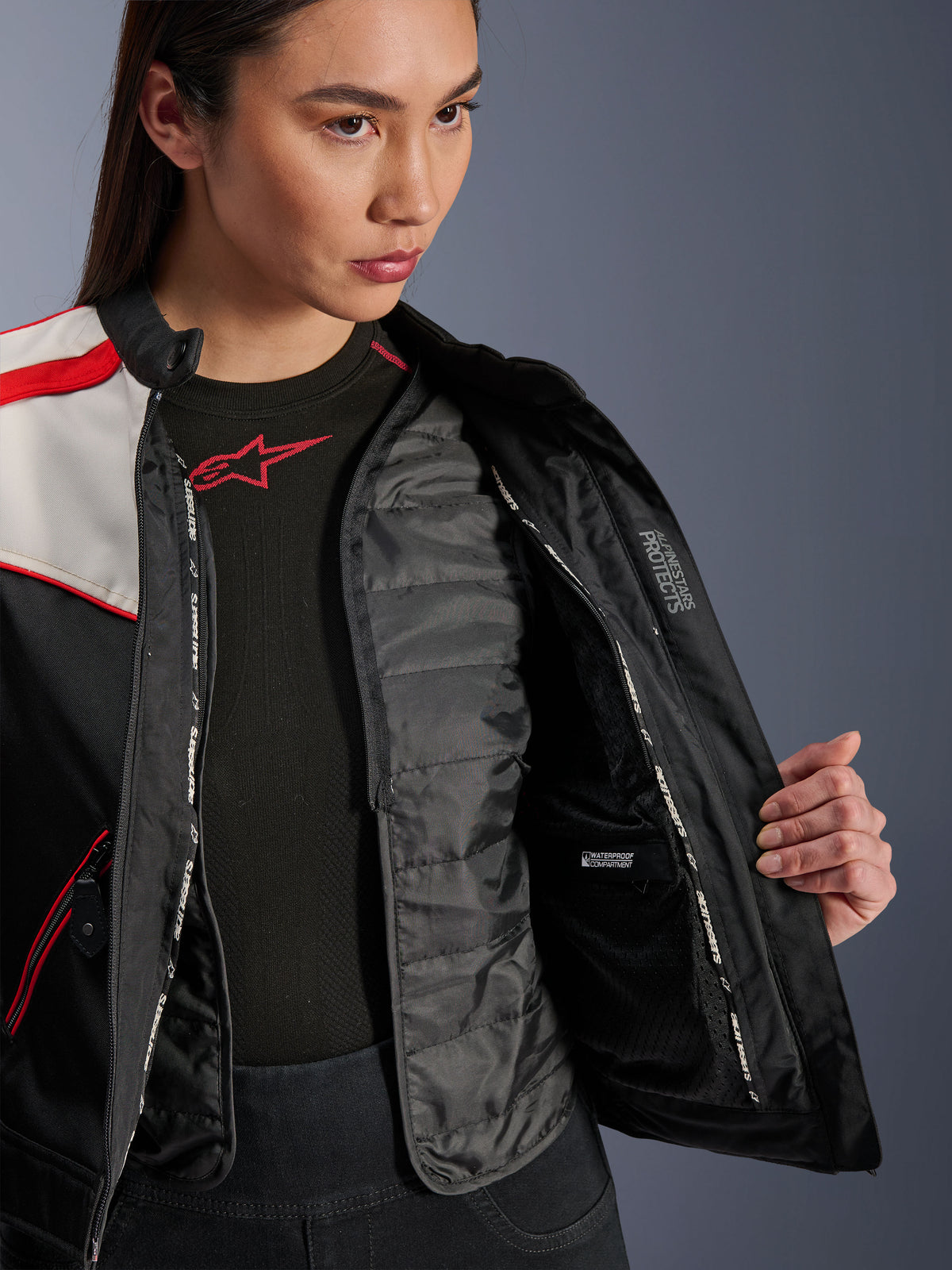 Casaco Alpinestars Stella T-Dyno WR, casaco de motociclismo para mulher, preto, cru e vermelho vivo, vista interior em pormenor a mostrar o colete térmico acolchoado amovível, compartimento interno impermeável e a marcação 'ALPINESTARS PROTECTS'.