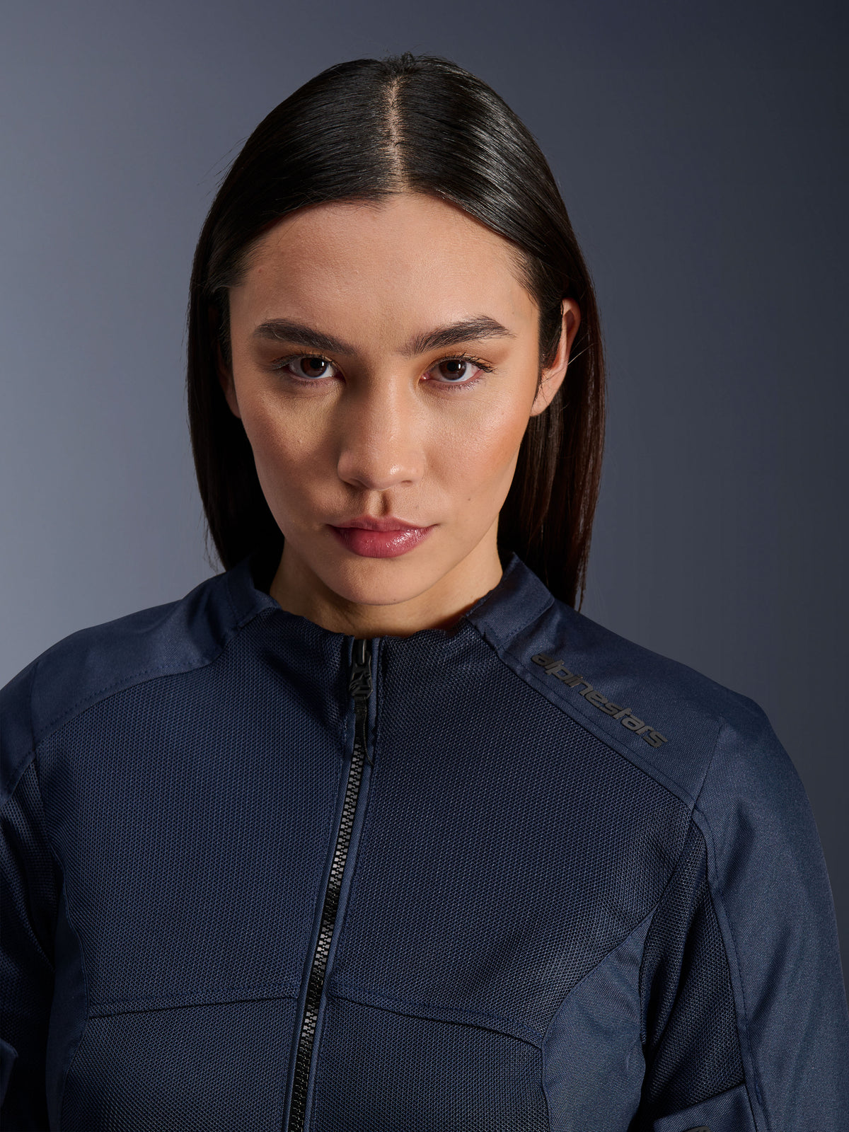 Modelo feminina a usar o casaco Alpinestars Stella C-1 Air em azul escuro, plano aproximado que mostra a textura de malha respirável, fecho de correr frontal e logótipo Alpinestars na gola, vestuário de motociclismo urbano e elegante