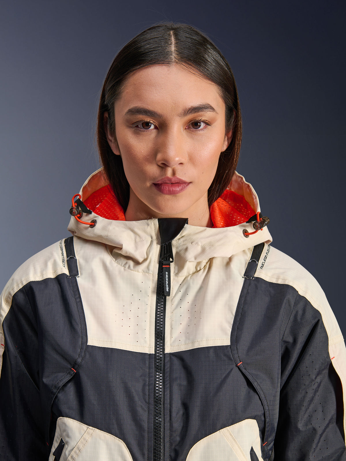Alpinestars Molly Air Jacket, casaco de motociclismo têxtil para senhora, Black Almond, vista frontal em grande plano de uma modelo a usar o casaco com design de painéis creme e preto, capuz com forro em malha cor de laranja vibrante e detalhes perfurados a laser no peito