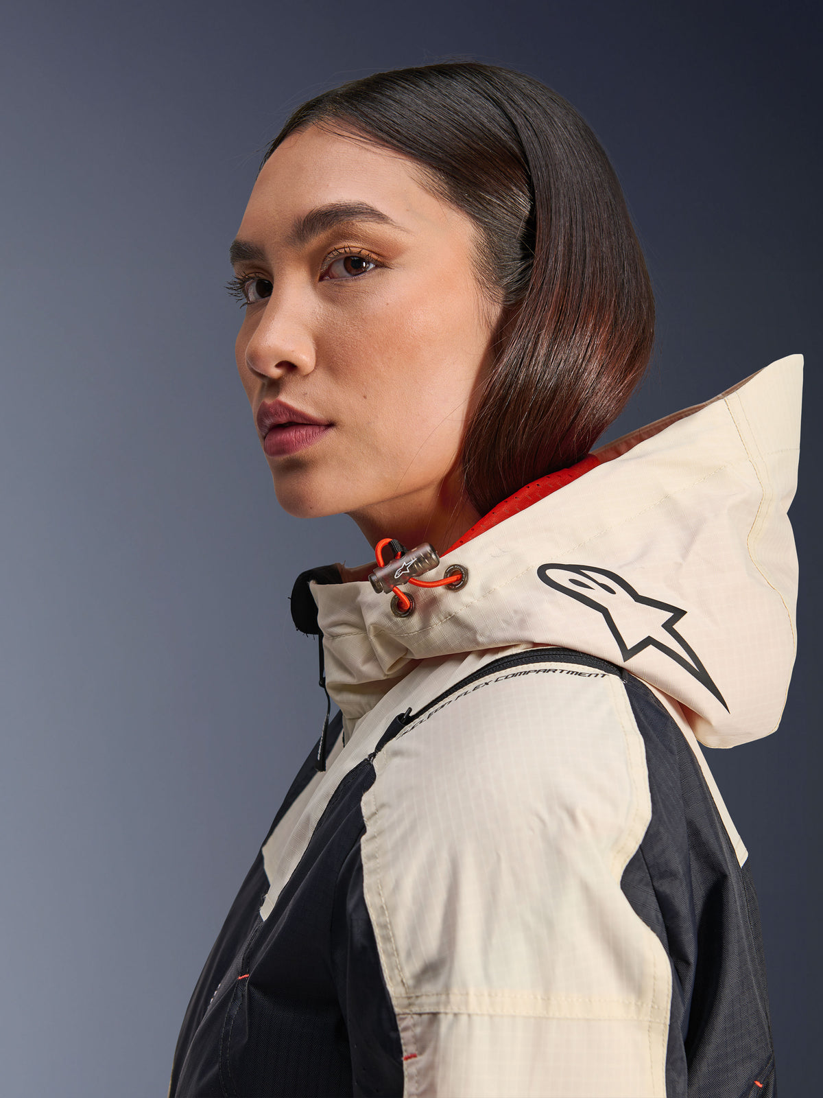 Alpinestars Molly Air Jacket, Black Almond, casaco de motociclismo urbano contemporâneo, vista de perfil lateral de modelo a usar o capuz com logótipo Alpinestars e detalhes em cordão cor de laranja, textura de tecido ripstop
