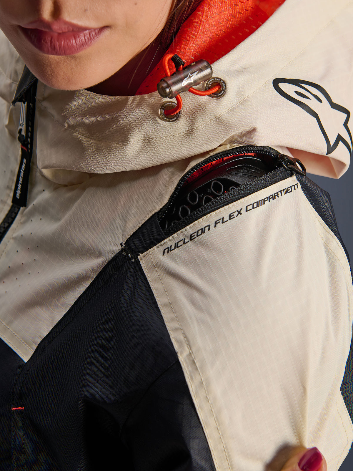 Alpinestars Molly Air Jacket, casaco de motociclismo para mulher, Black Almond, vista de pormenor do ombro mostrando o fecho do Nucleon Flex Compartment, tecido ripstop e forro em malha laranja no interior do capuz