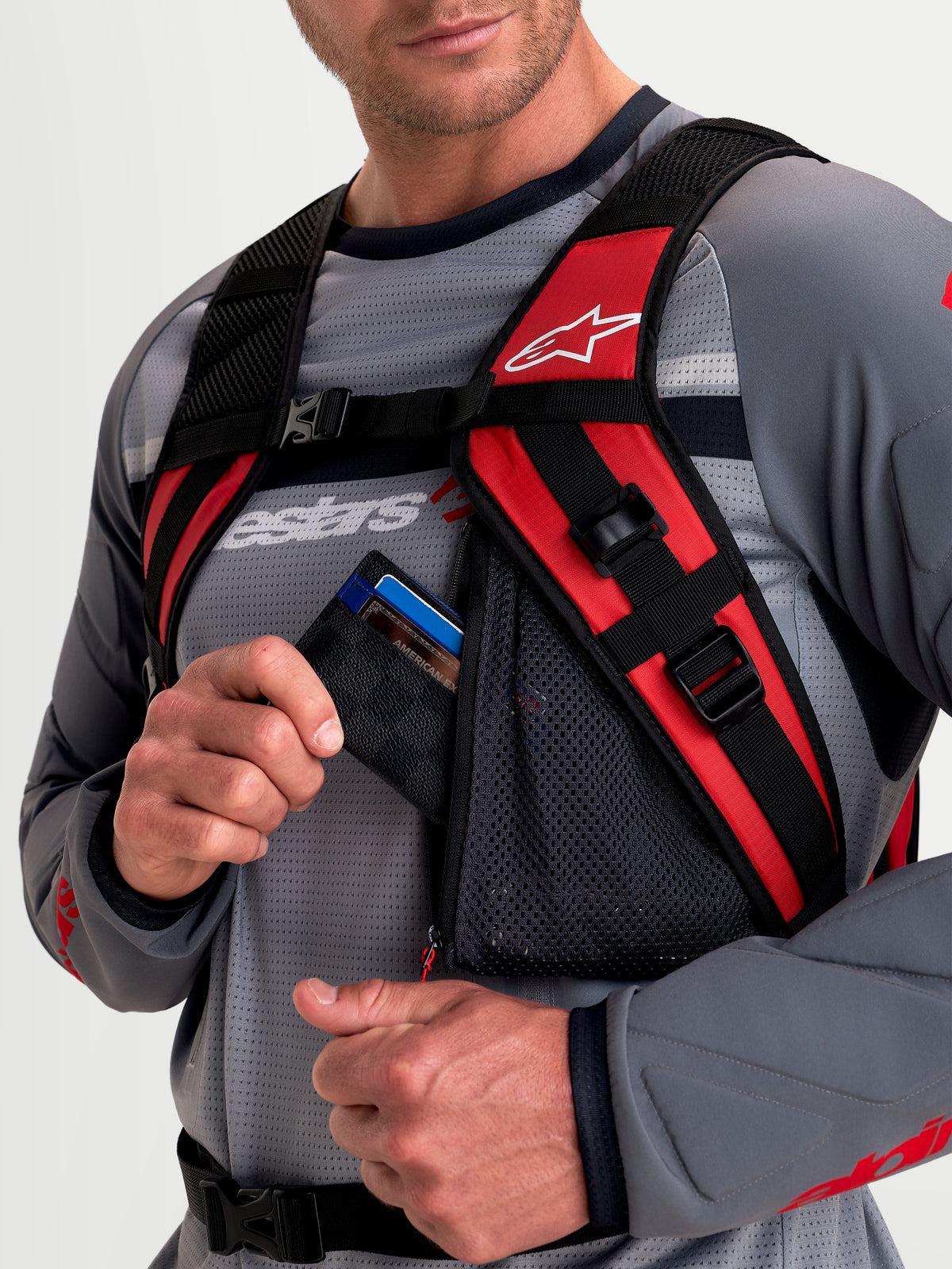 Alpinestars Mochila AT-9, mochila de motocross para homem, preto e vermelho vivo, vista de pormenor a mostrar o sistema de alças de ombro almofadadas e o bolso de rede com fecho de correr num modelo