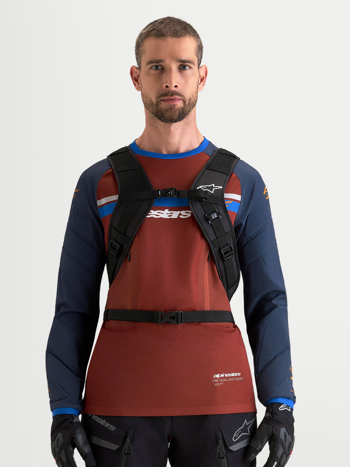 Mochila Alpinestars AT-9, mochila de motocross preta e cinzenta-escura, vista frontal num modelo masculino com alças almofadadas e sistema de fecho com fivela no peito