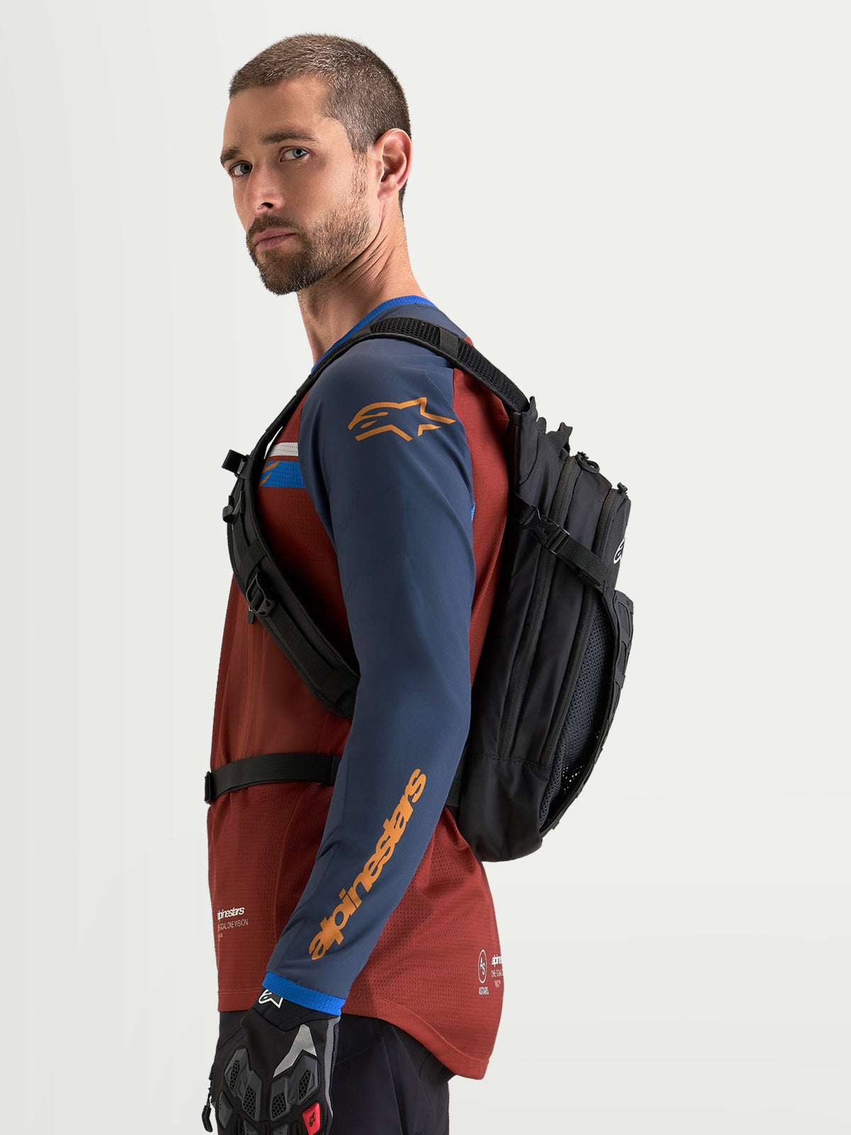 Alpinestars Mochila AT-9, mochila de motocross para utilização diária, preta, vista lateral num modelo com equipamento de condução