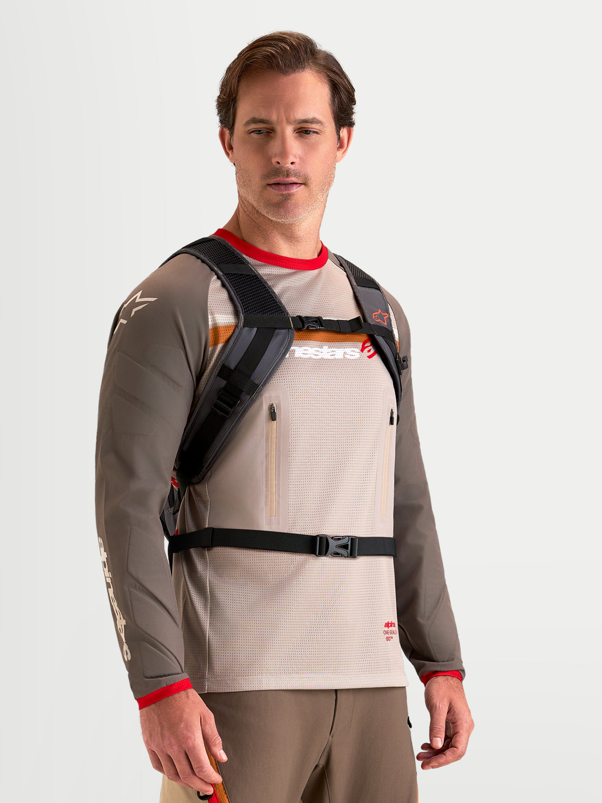 Alpinestars AT-9 Back Pack, motocross backpack in walnut and deep gray, worn by a male model showing the padded shoulder harness and buckled strap closure system, lightweight textile construction