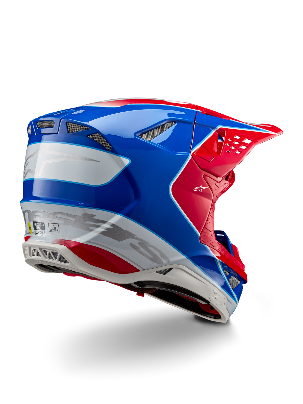 Capacete Alpinestars Supertech M10 Aeon ECE 22.06, capacete de motocross, vermelho brilhante, azul e branco com acabamento brilhante, vista lateral traseira com perfil aerodinâmico, logótipo Alpinestars prateado e aberturas de ventilação integradas.