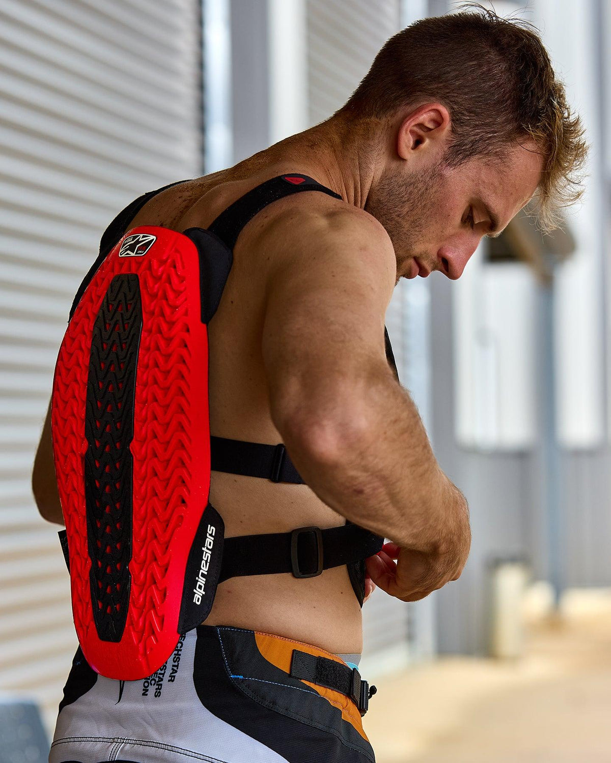 Alpinestars A-5 Plasma Chest Protector, Red and Black, featuring a textured back protector with Nucleon PLASMA technology, worn by a man adjusting black straps, side view highlighting the protective shell and flexible design for off-road riding