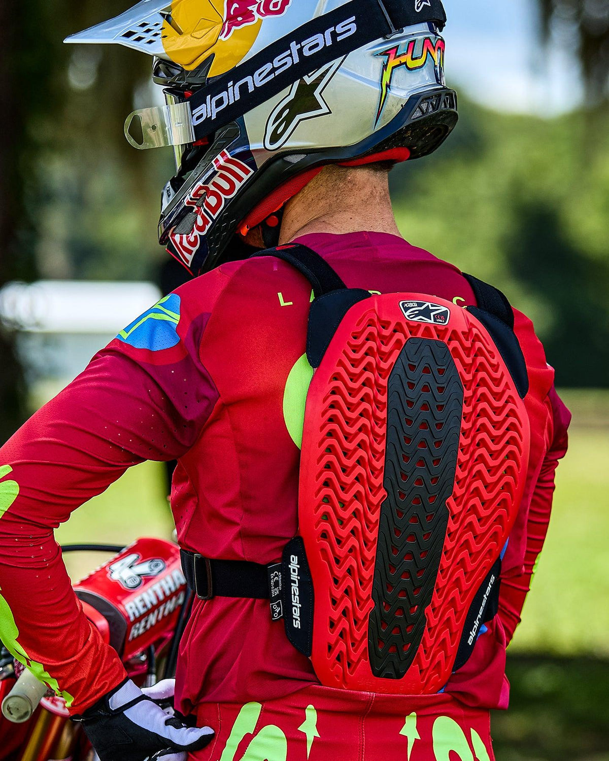 Motocross rider seen from behind wearing the Alpinestars A-5 Plasma Chest Protector, featuring a red and black back protector with a ventilated honeycomb structure, worn over a red long-sleeve jersey with a Red Bull branded helmet.